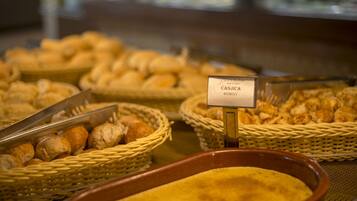 Un bufé con diversas opciones de productos horneados, como pan y pasteles, exhibidos en cestas de mimbre y un recipiente de cerámica.