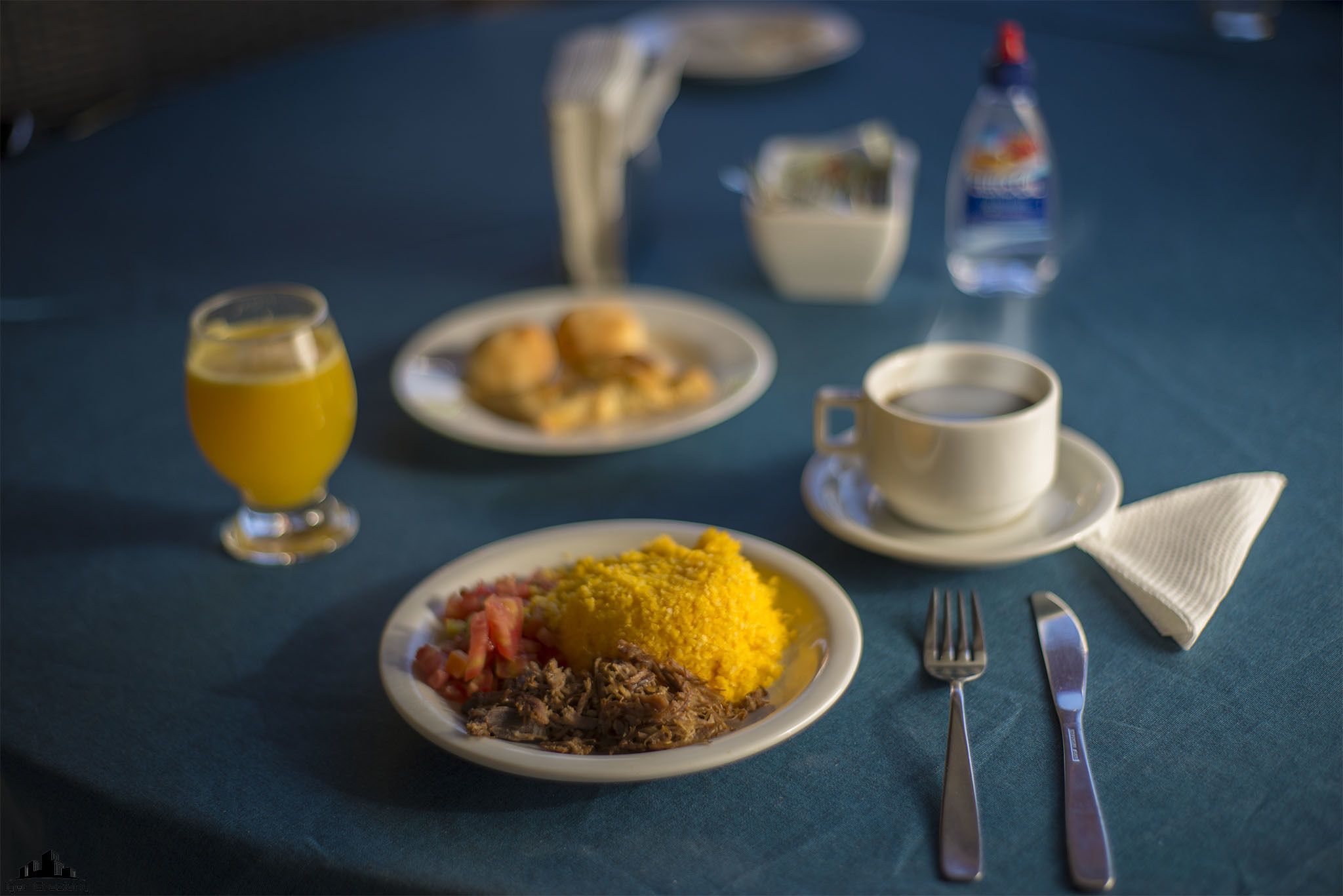 A table with plates of food, a glass of juice, a cup of coffee, and a bottle of water.