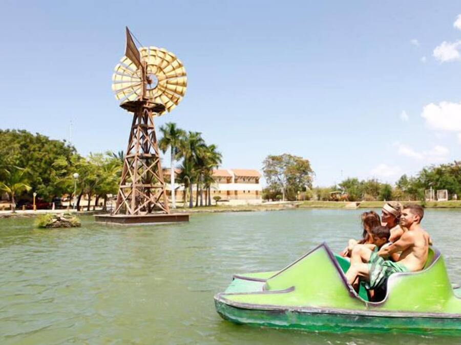 Un bote verde con pasajeros, un molino y un edificio al fondo.