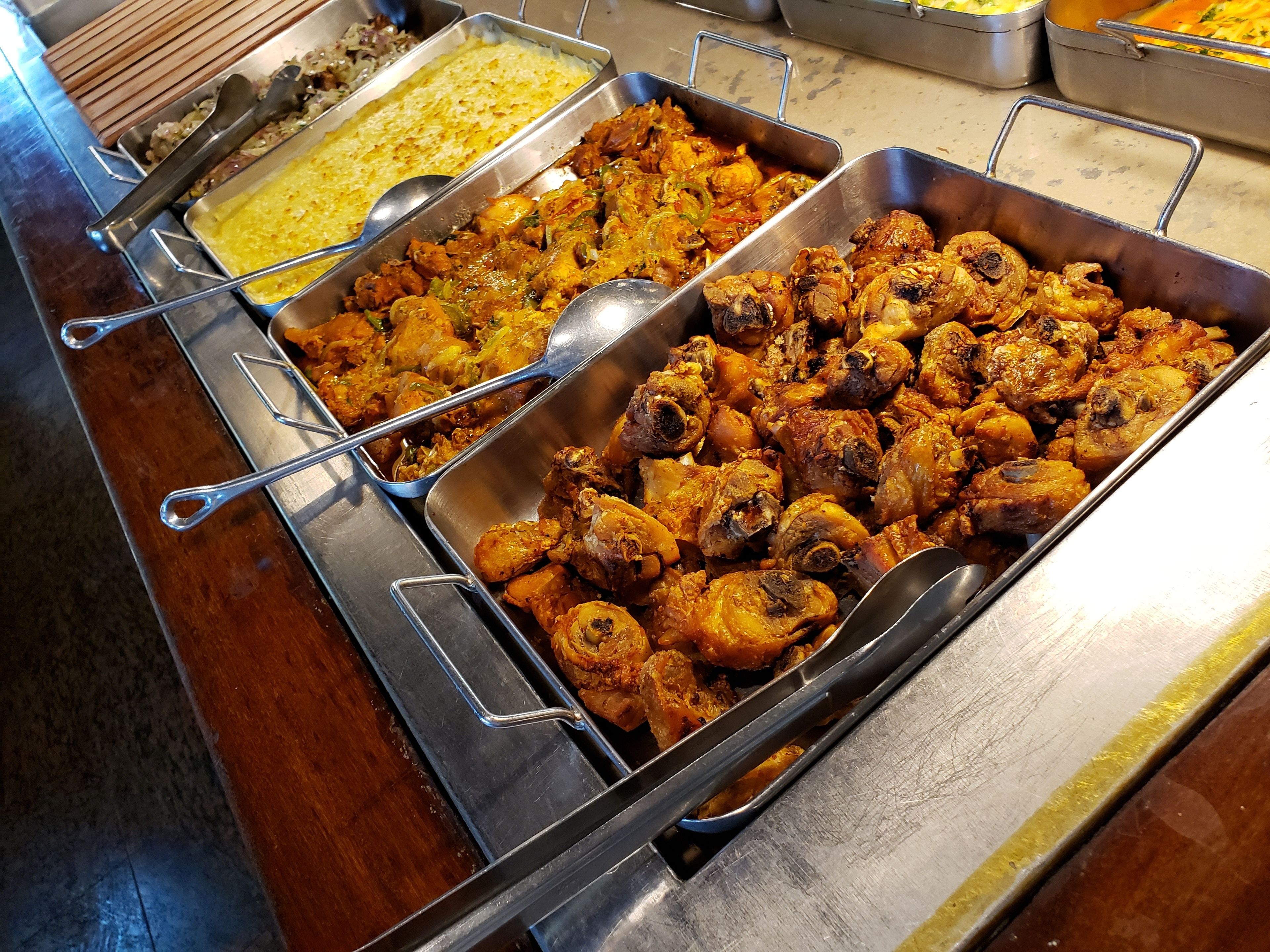 A buffet with various dishes including roasted chicken and a yellow rice dish.