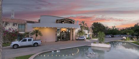 A hotel with a pool, a white pickup truck parked in front, and a sunset sky.