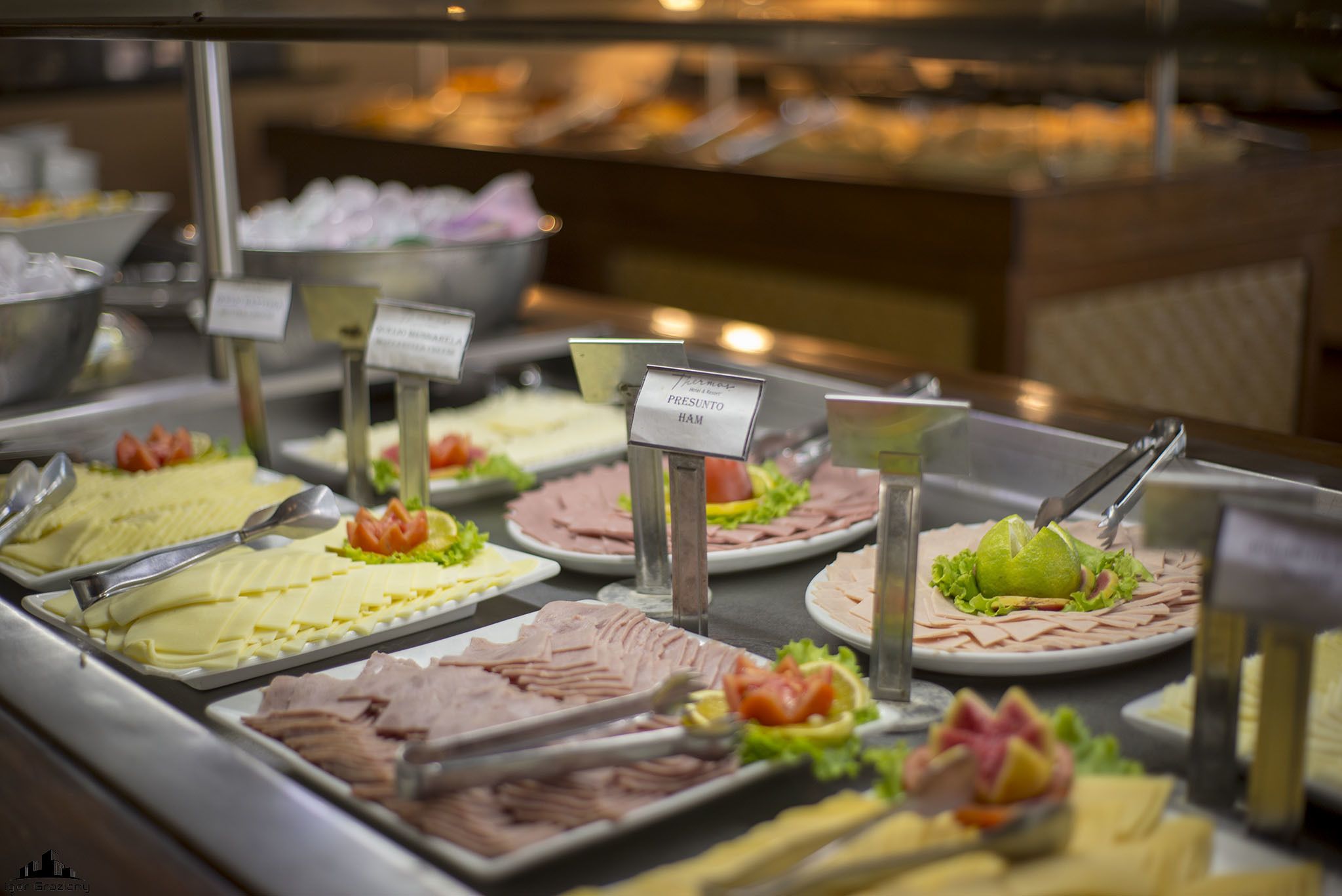 Un bufé con diversos alimentos, como jamón y queso, dispuestos en bandejas con etiquetas.