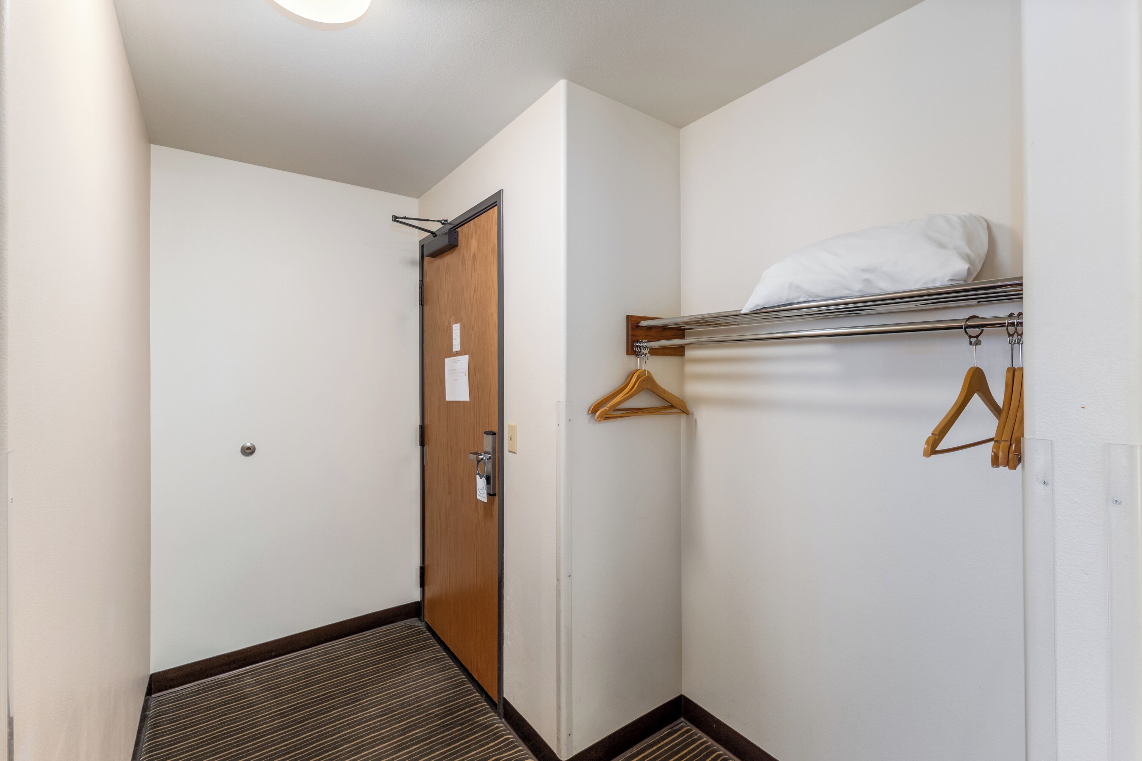 A hotel hallway with a wooden door, a coat rack with hangers, and a white wall.