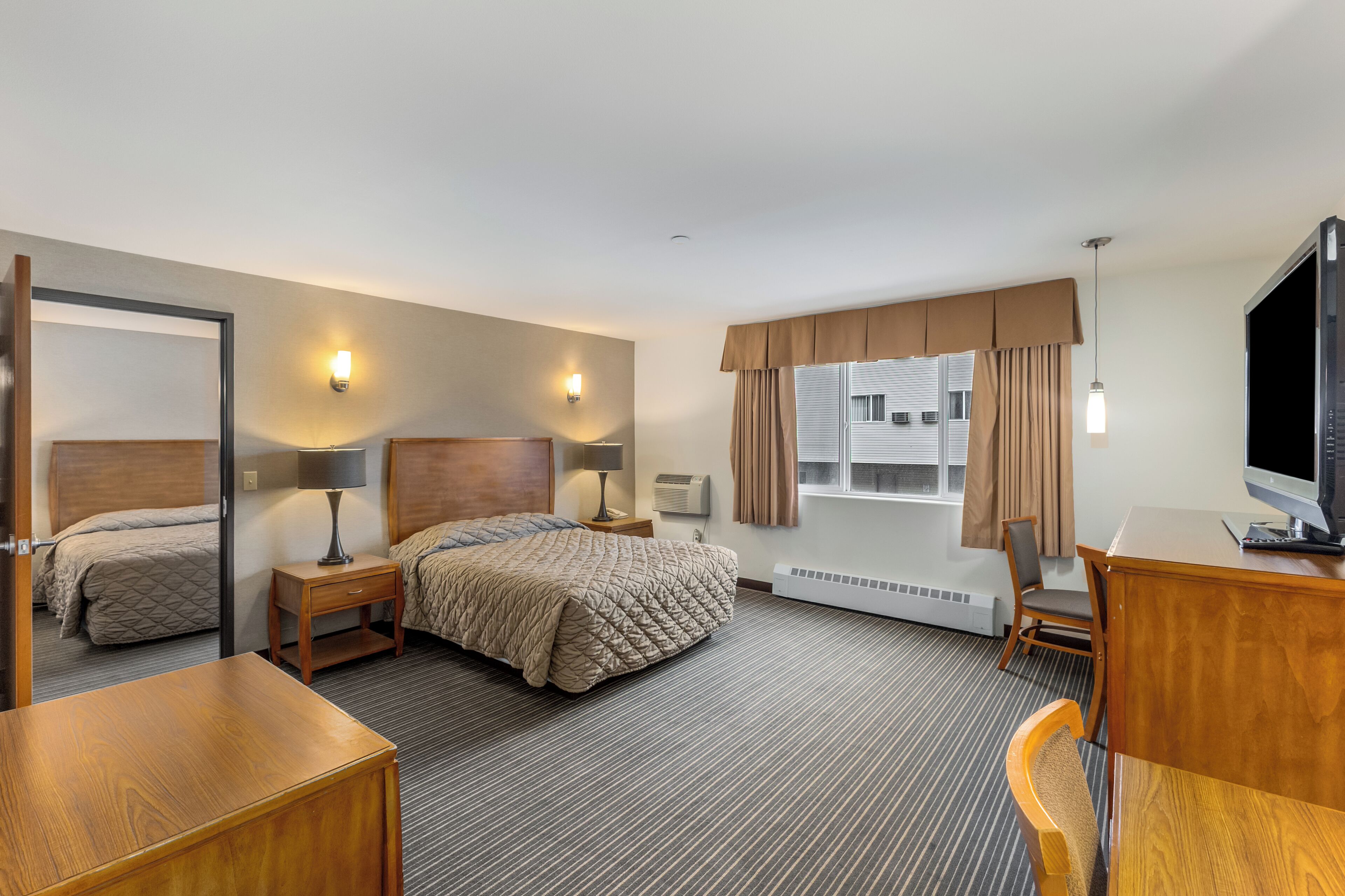 A hotel room with two beds, a desk, a chair, a TV, and a window with curtains.
