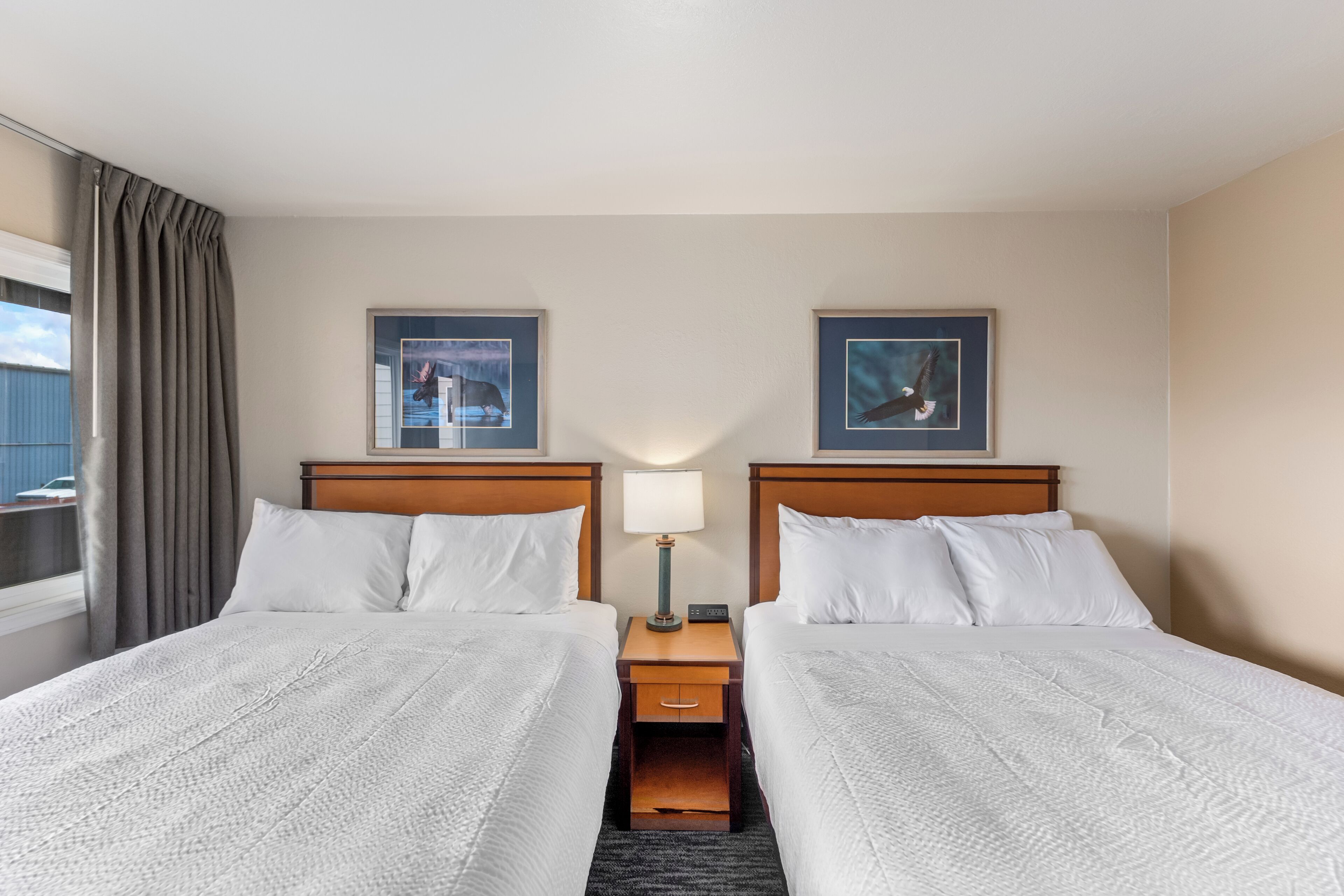 A hotel room with two beds, a nightstand with a lamp, and two framed pictures on the wall.