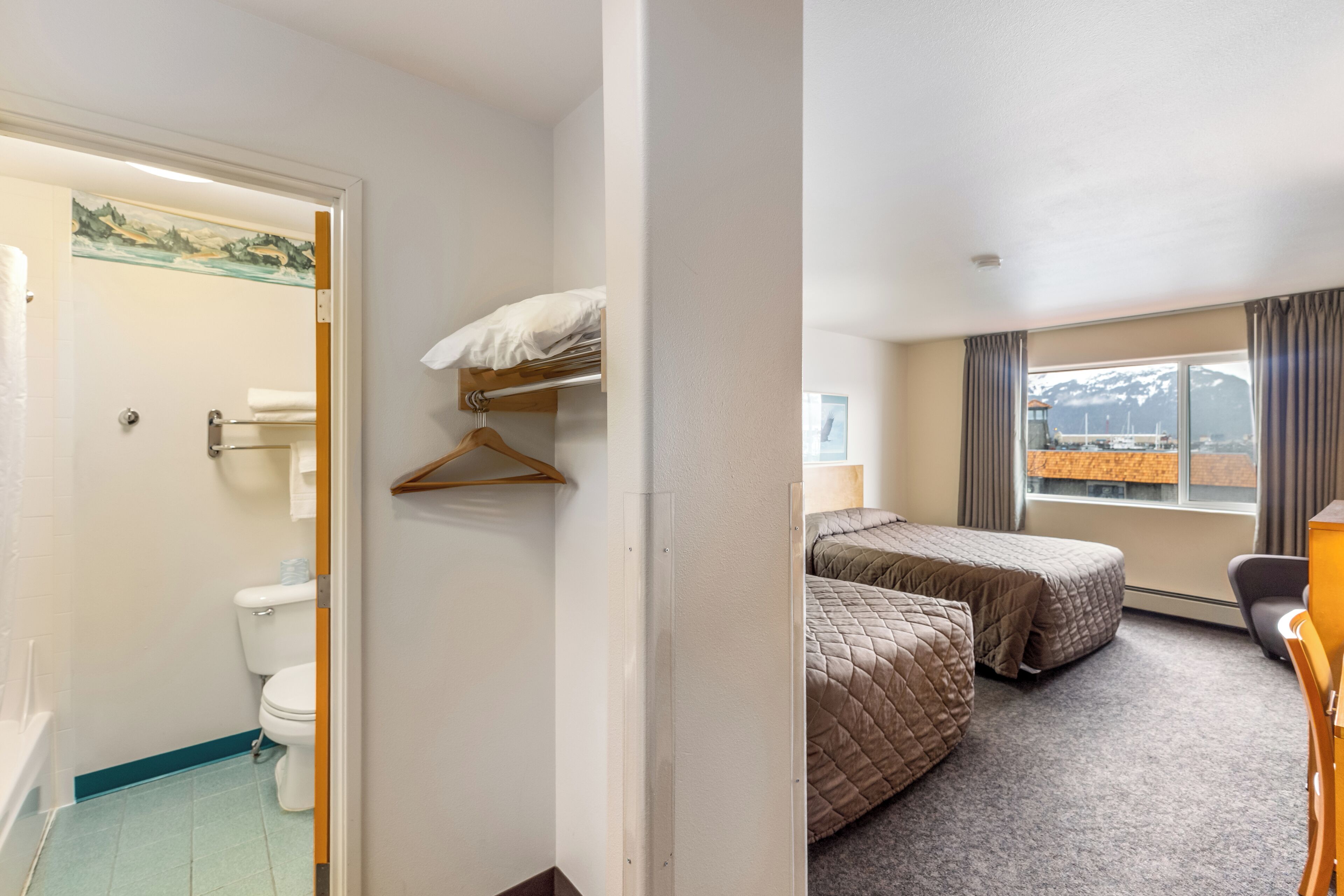 A hotel room with a bathroom, two beds, a window with a view, and a desk.