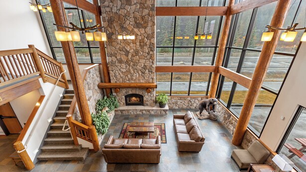 A spacious living area with a stone fireplace, a wooden staircase, and large windows offering a view of the outdoors.
