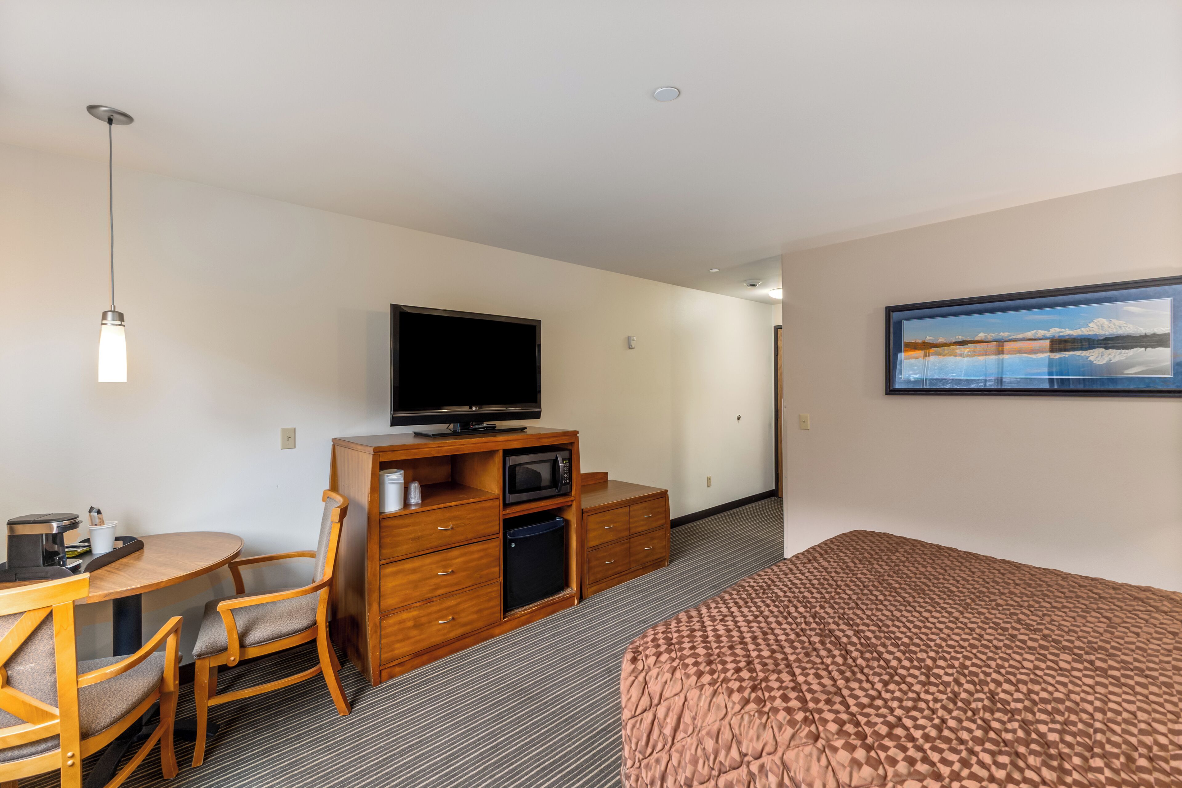 Una habitación de hotel con una cama, un escritorio con una silla, un televisor, un microondas y un aparador.