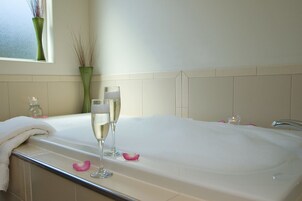 A bathroom with a large bathtub, two champagne glasses, a vase with dried plants, and a window with a view.