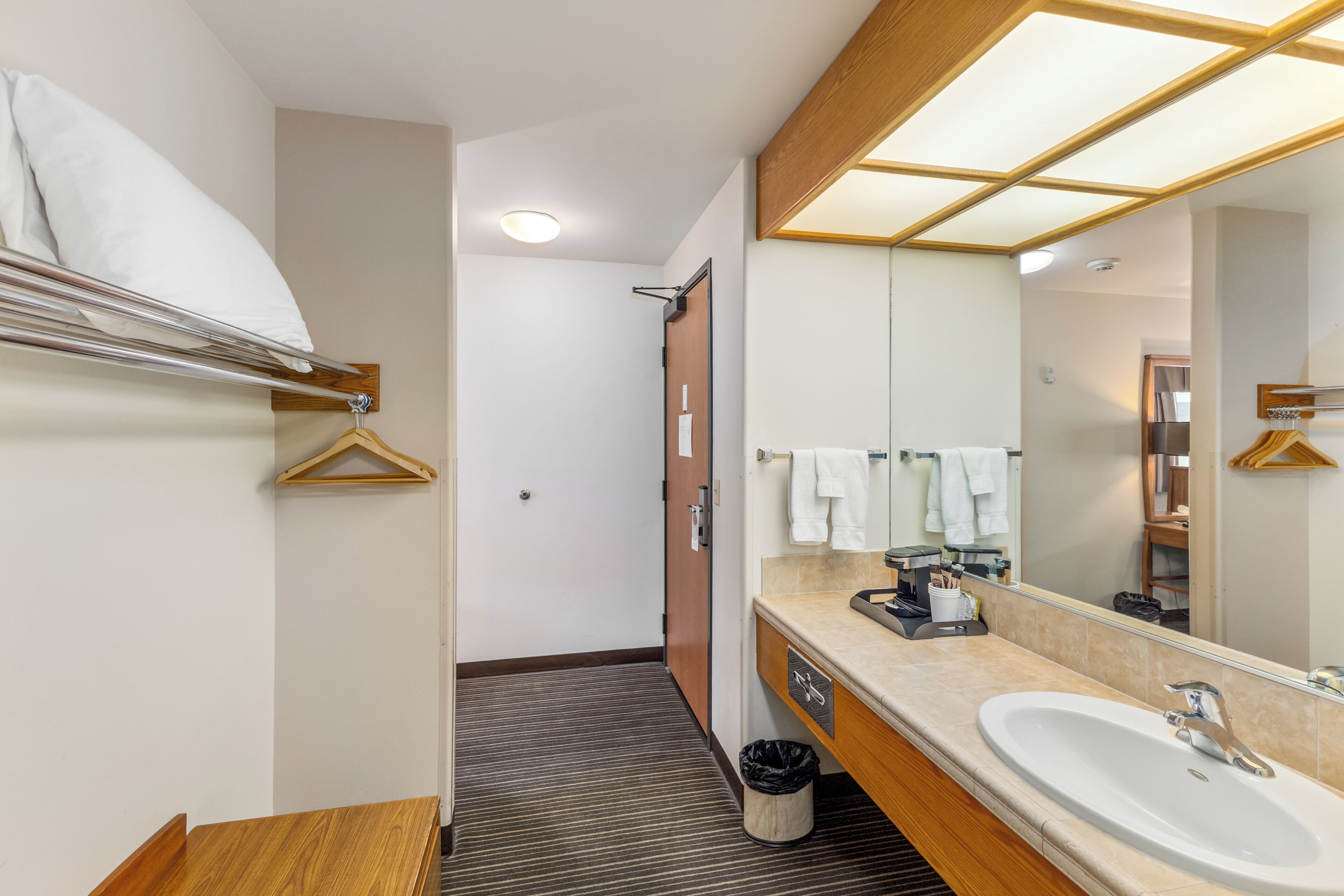A modern hotel bathroom with a large mirror, a sink, and a wooden vanity.