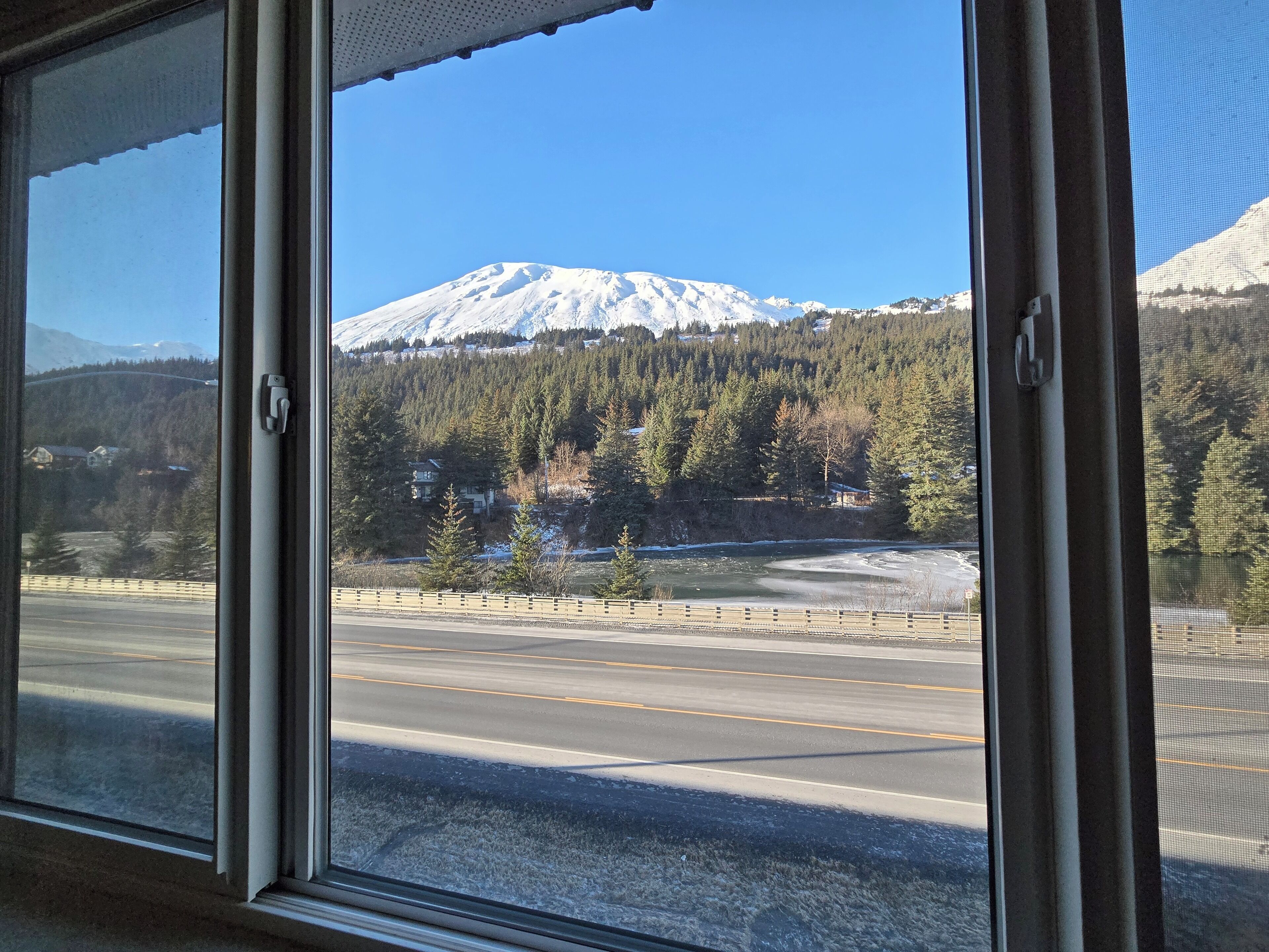 A view through a window of a road with a snow-covered mountain in the background.