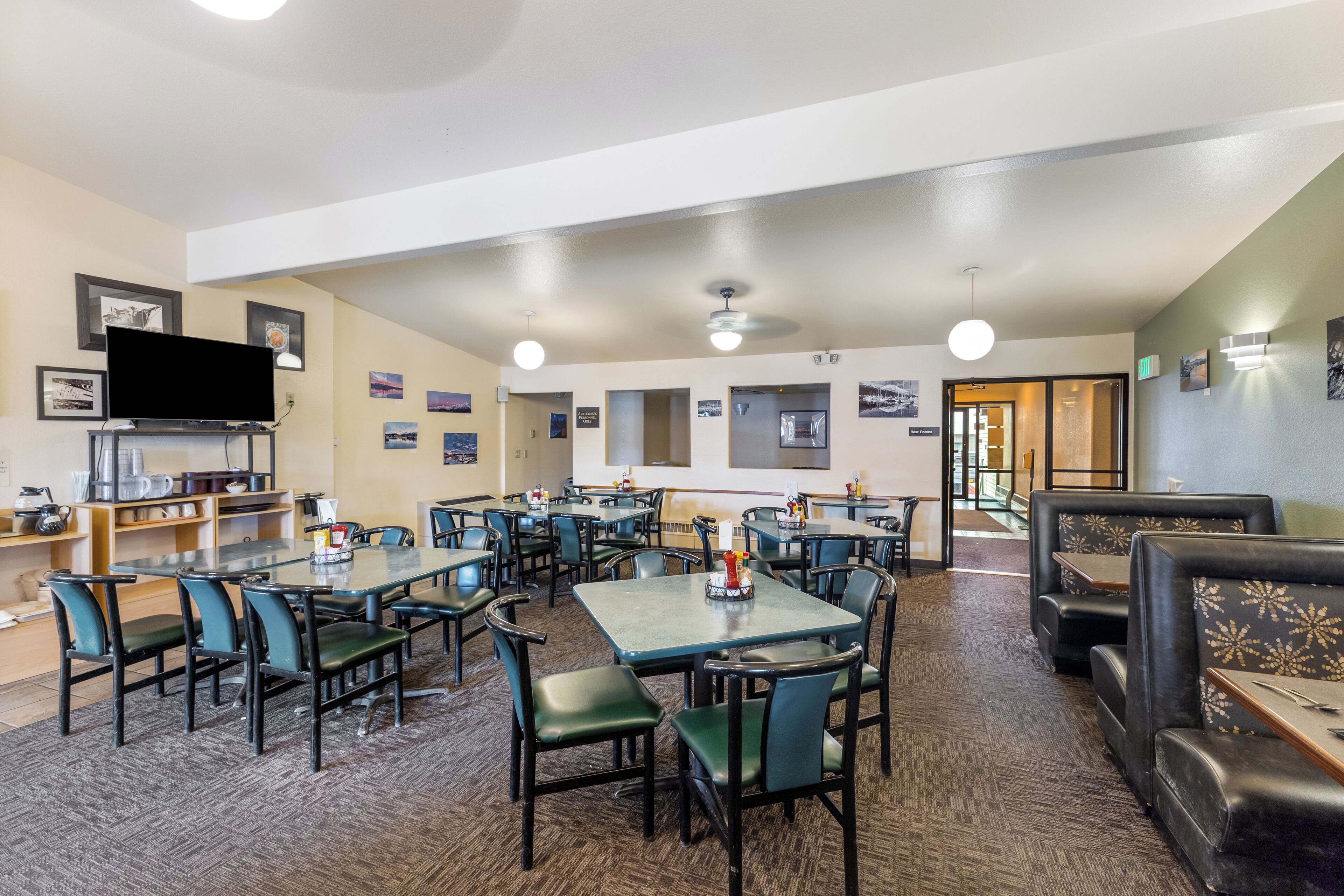 A spacious restaurant with multiple tables and booths, a flat-screen TV mounted on the wall, and framed pictures on the walls.