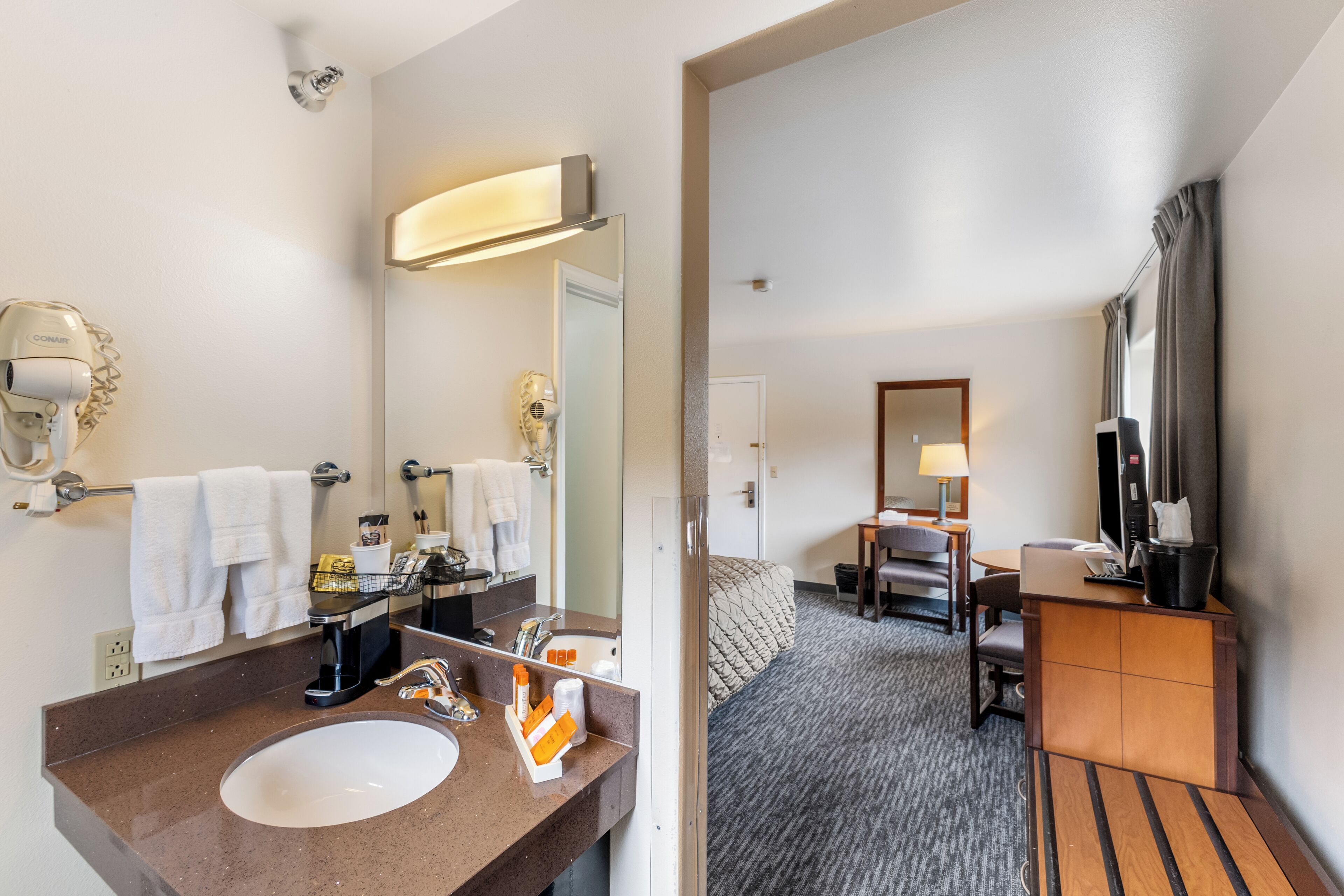 Ein Hotelbad mit Waschbecken, Spiegel, Handtuchhalter und Pflegeprodukten.