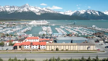 Una marina con numerose imbarcazioni ormeggiate, una grande nave da crociera e montagne innevate sullo sfondo.
