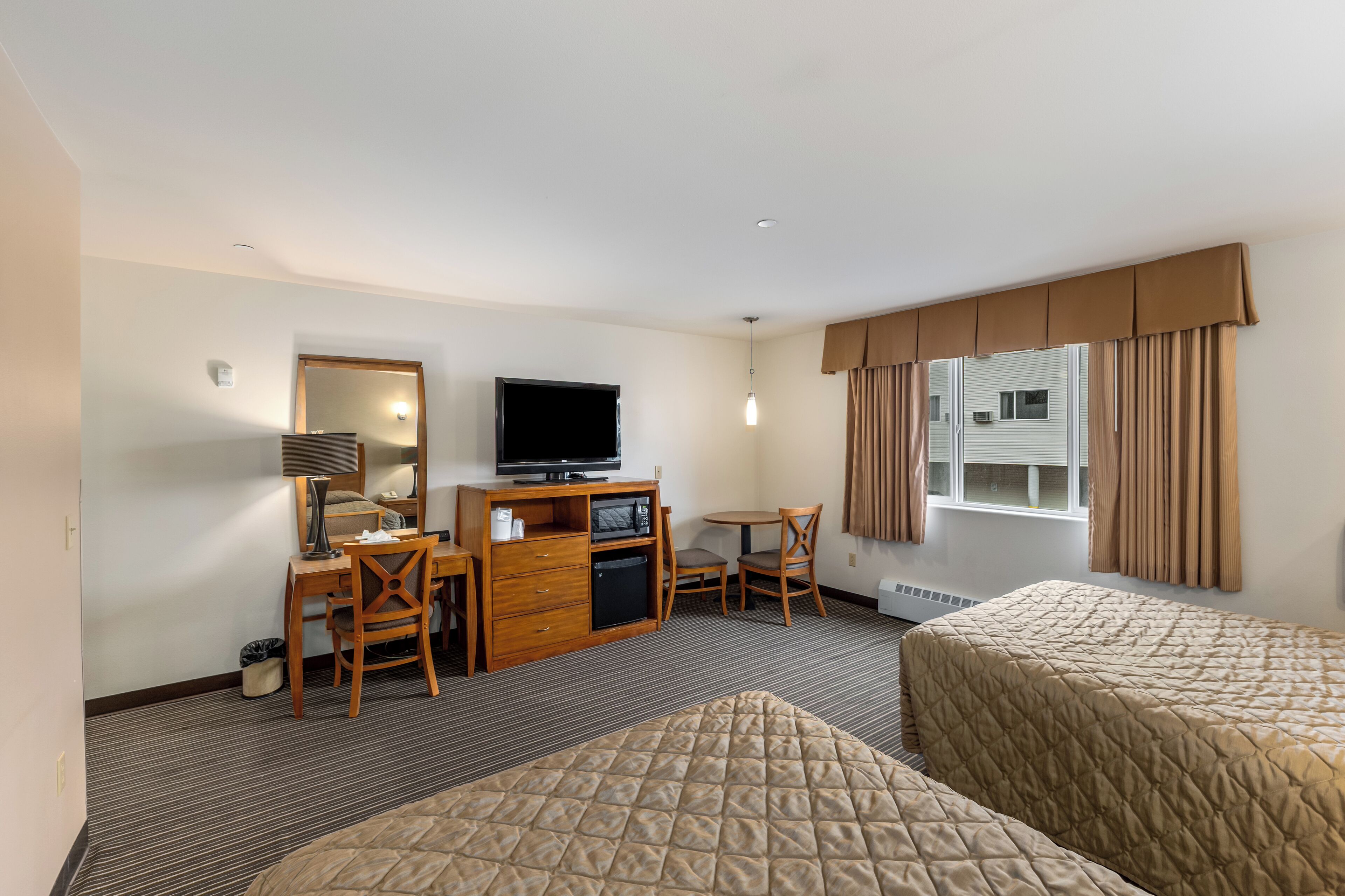 Une chambre d’hôtel avec deux lits, un bureau avec une télévision, une chaise et une petite kitchenette.