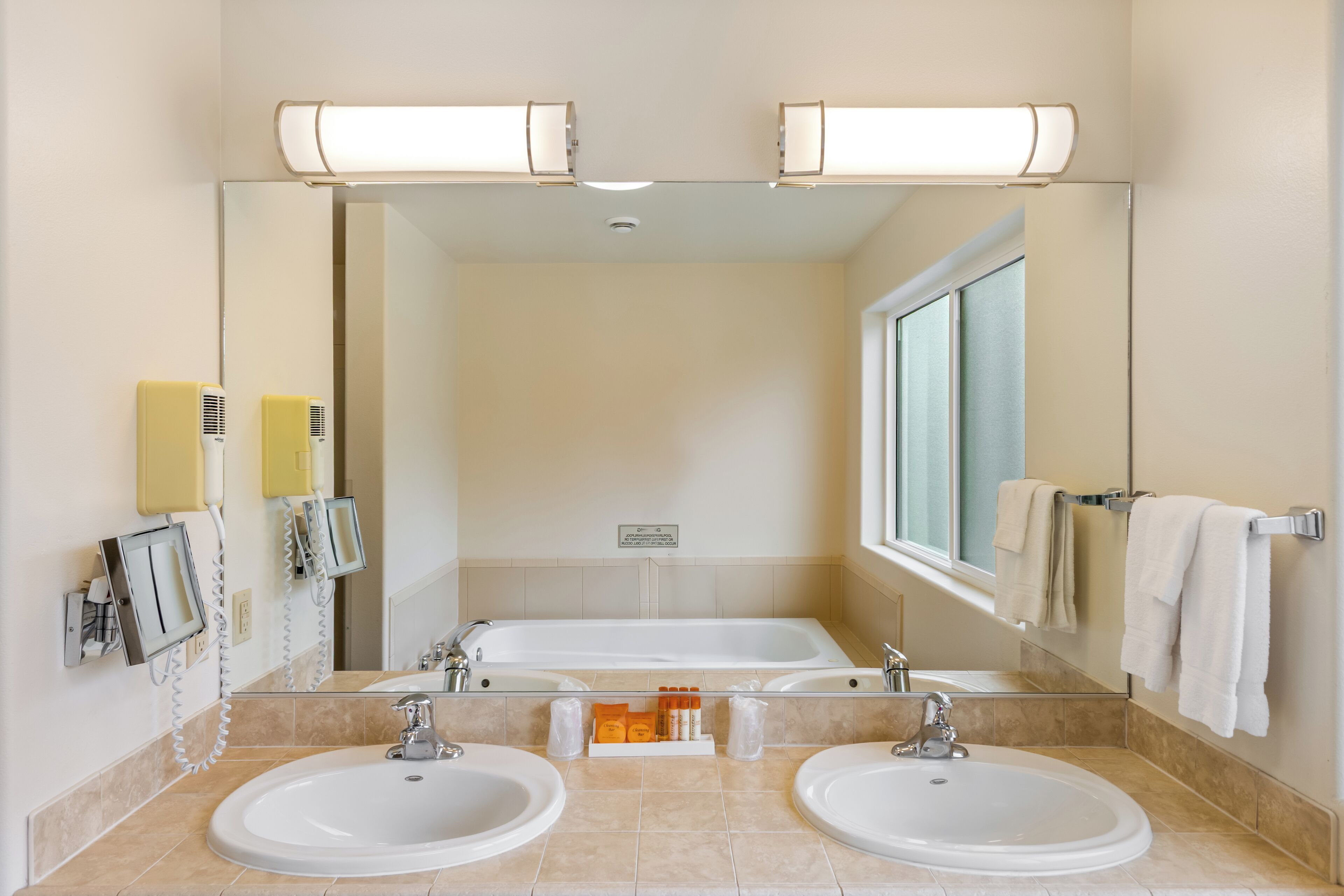 Un baño de hotel con dos lavamanos, un espejo grande y una ventana.