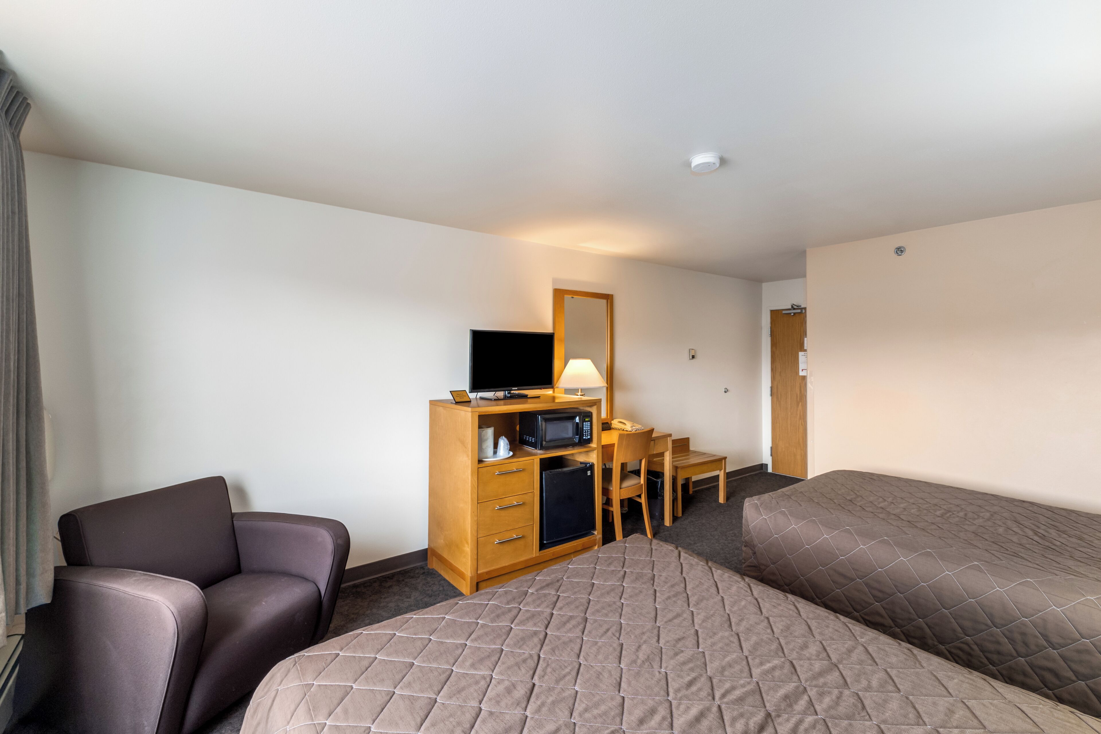 A hotel room with two beds, a desk with a television, a refrigerator, and a chair.