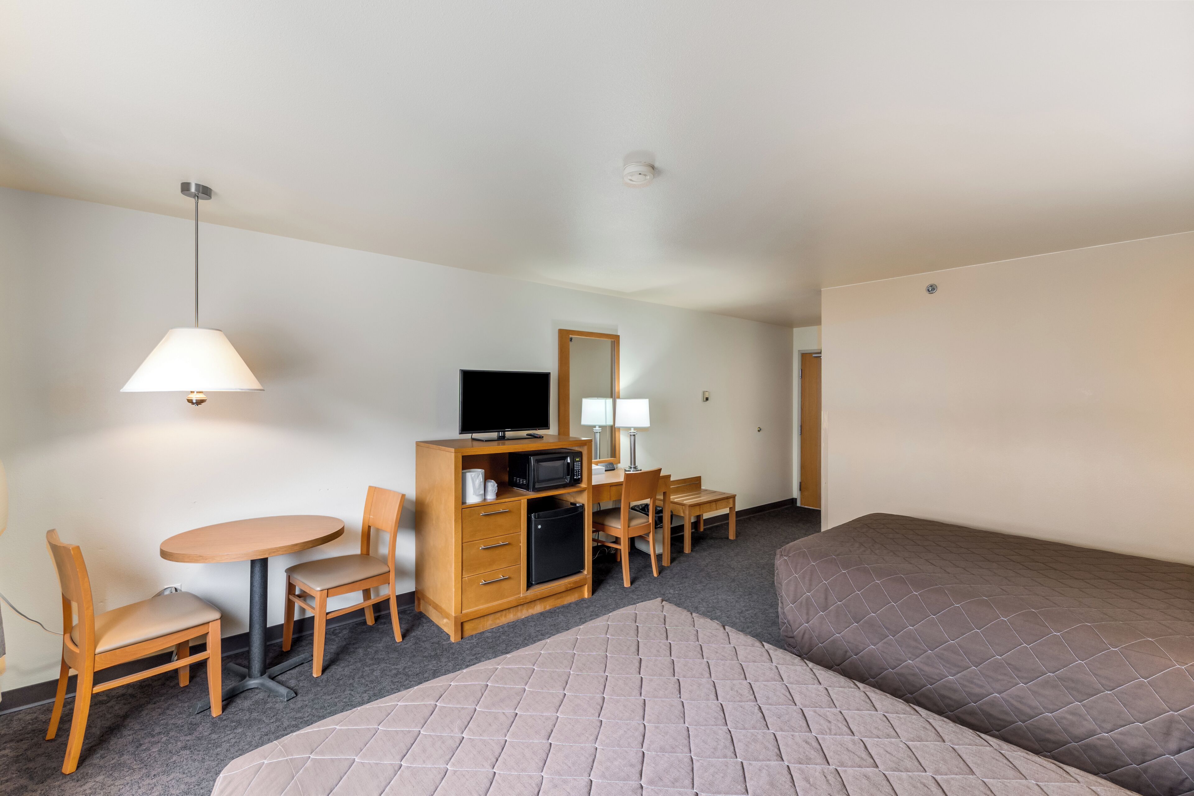 A hotel room with a bed, a desk with a computer, a microwave, a small refrigerator, a TV, and a lamp.