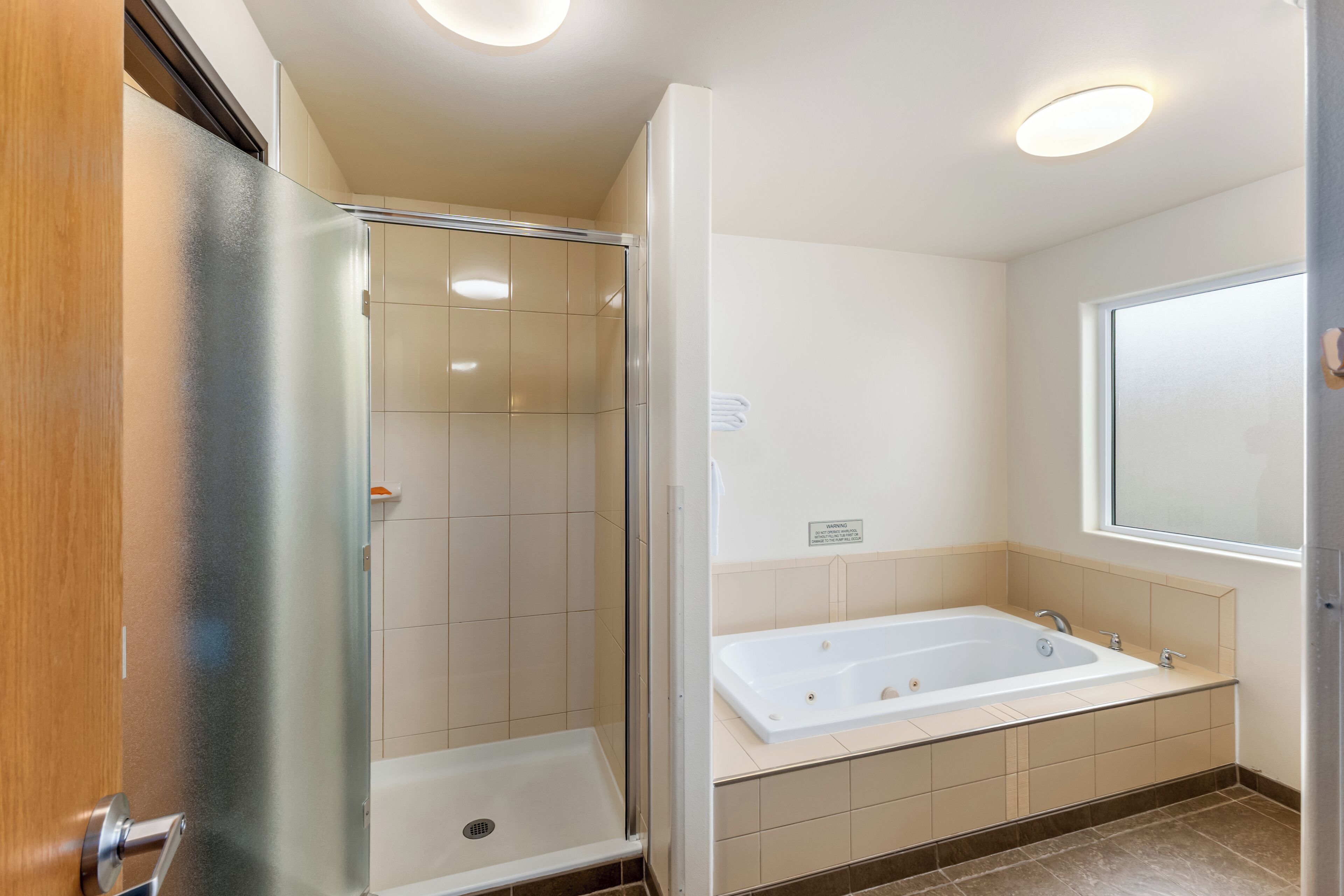 Een badkamer met een douche in een glazen cabine, een bad en een raam.