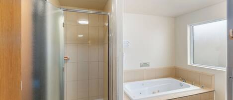 Een badkamer met een douche in een glazen cabine, een bad en een raam.