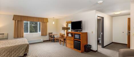 A hotel room with a bed, a desk with a chair, a television, a microwave, and a small refrigerator.