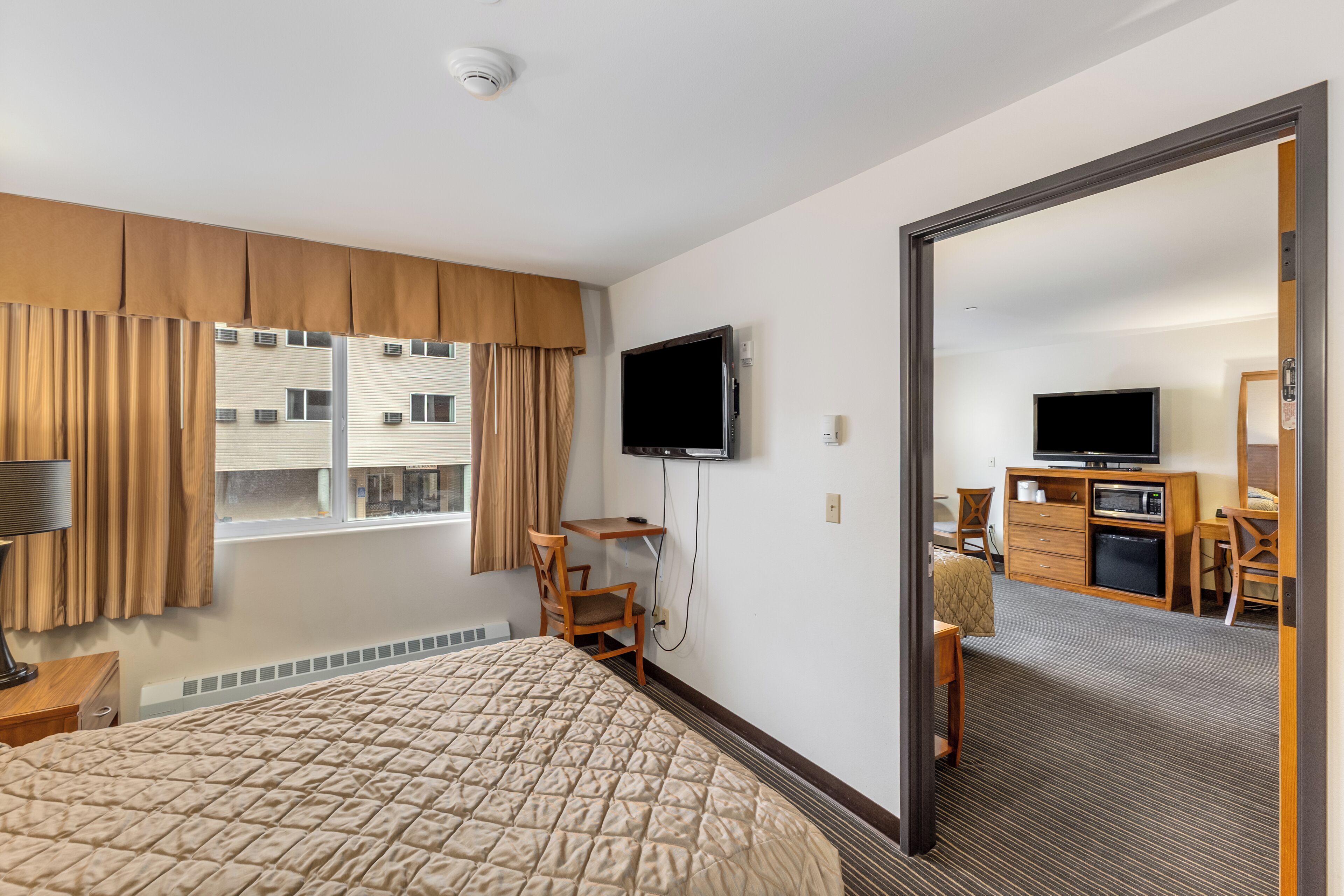 A hotel room with a large bed, a desk, a TV, and a view of the outside building.