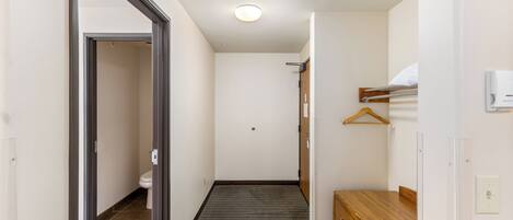 A narrow hallway with a wooden dresser, a hanging coat rack, and a door leading to a bathroom.