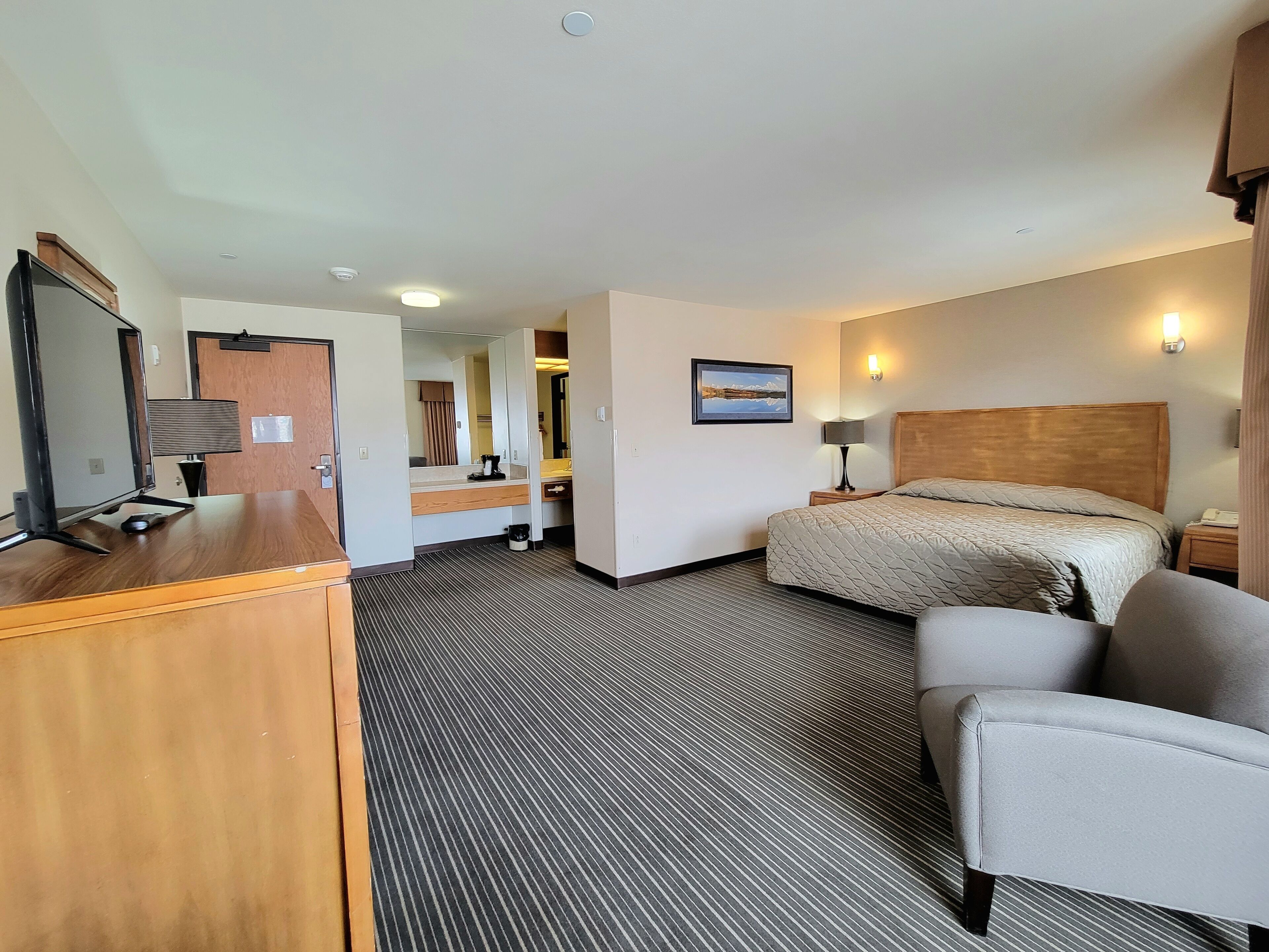 A hotel room with a bed, a desk with a computer, a chair, and a TV.