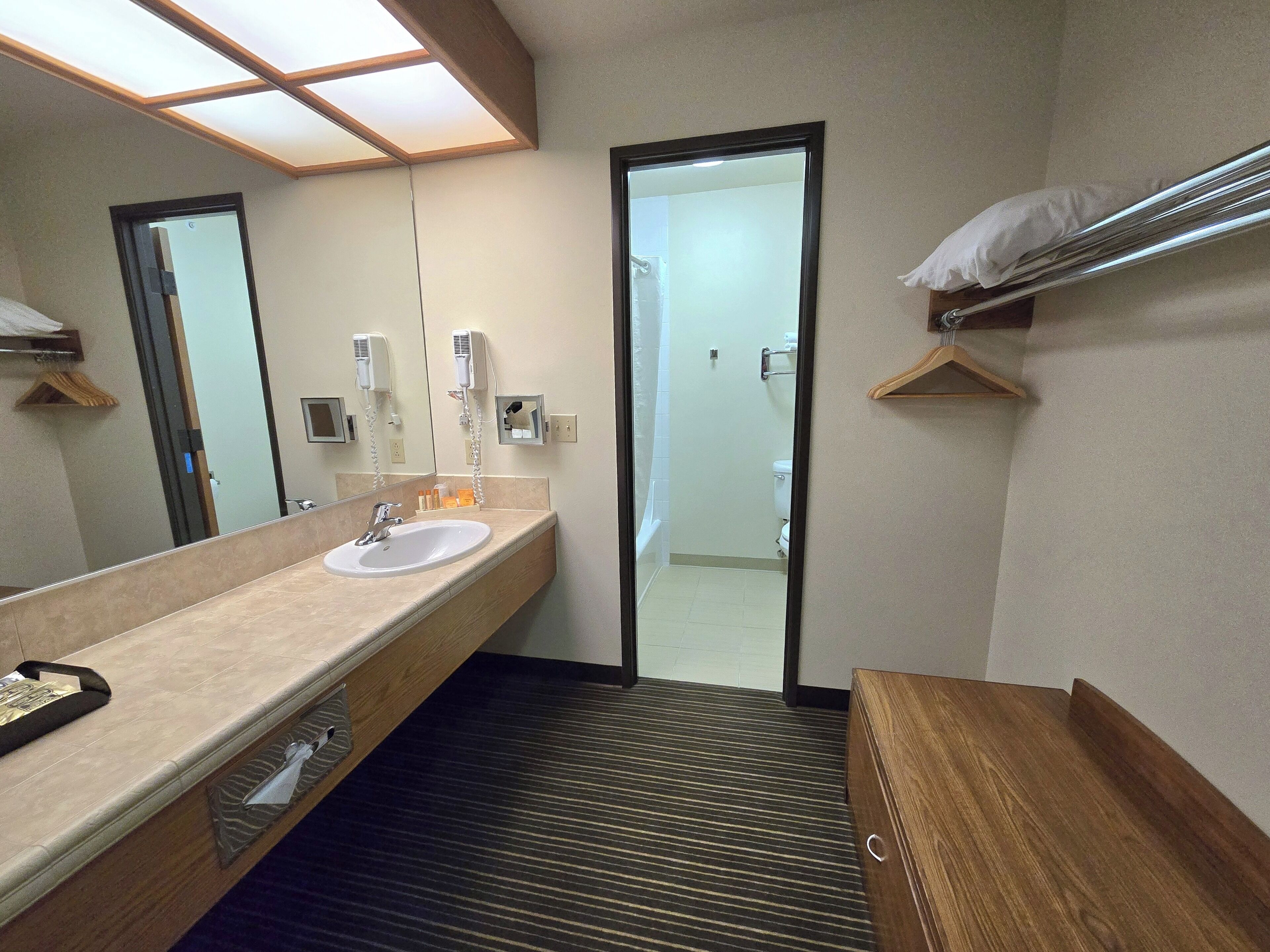 A hotel bathroom with a sink, mirror, towel rack, and a door leading to a shower area.
