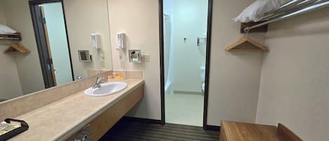 A hotel bathroom with a sink, mirror, towel rack, and a door leading to a shower area.