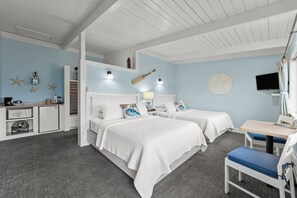 A bedroom with two beds, a desk, a chair, a TV, and a kitchenette.