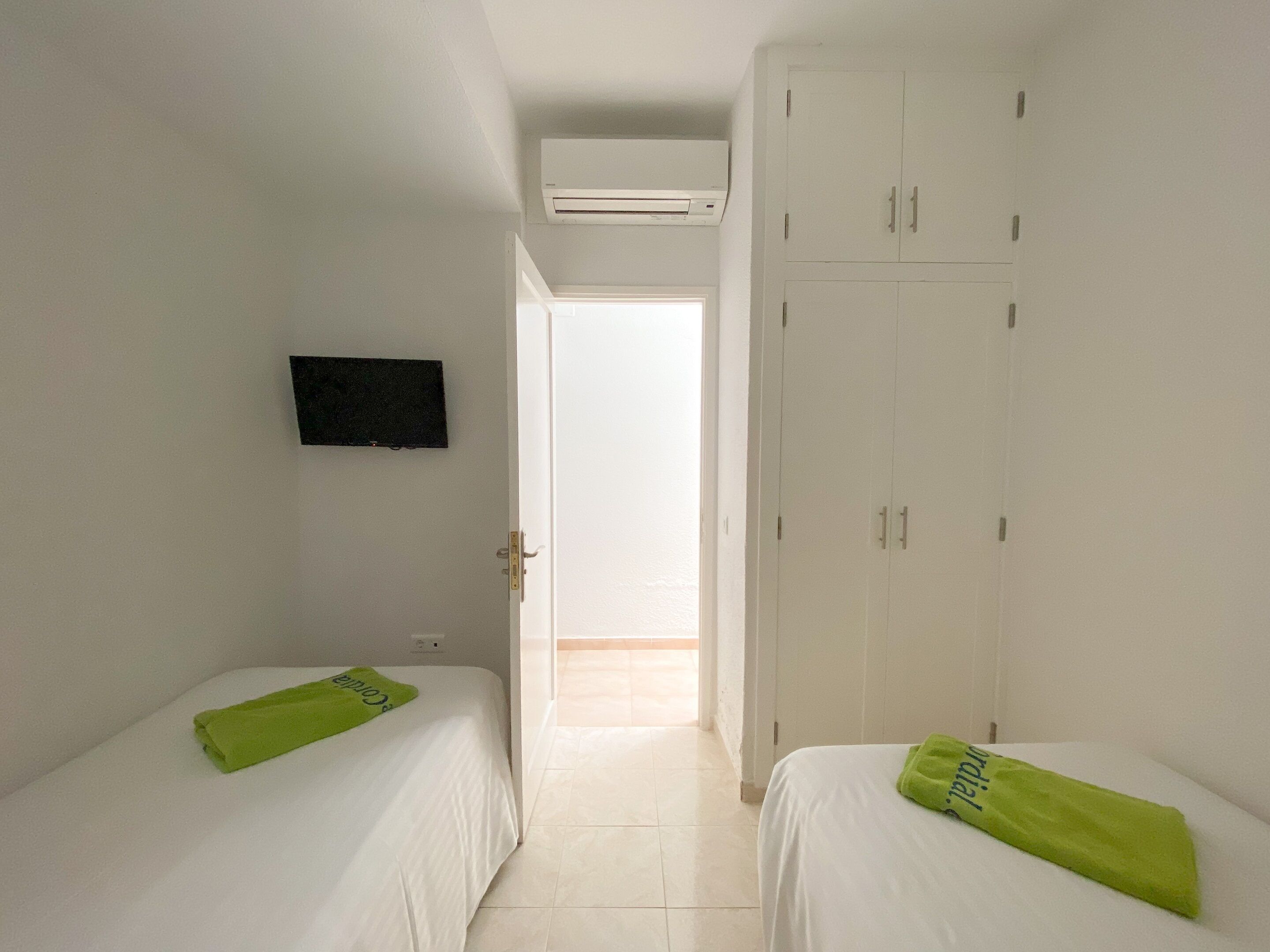 Una habitación de hotel con dos camas individuales, un televisor en la pared y un armario.