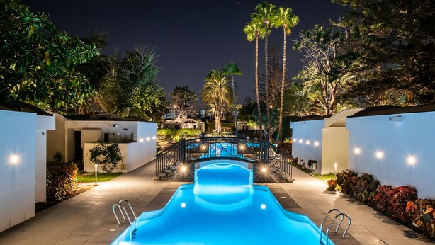 A swimming pool with a waterfall feature, surrounded by palm trees and a bridge. - Bungalows Cordial Biarritz (San Bartolomé de Tirajana)
