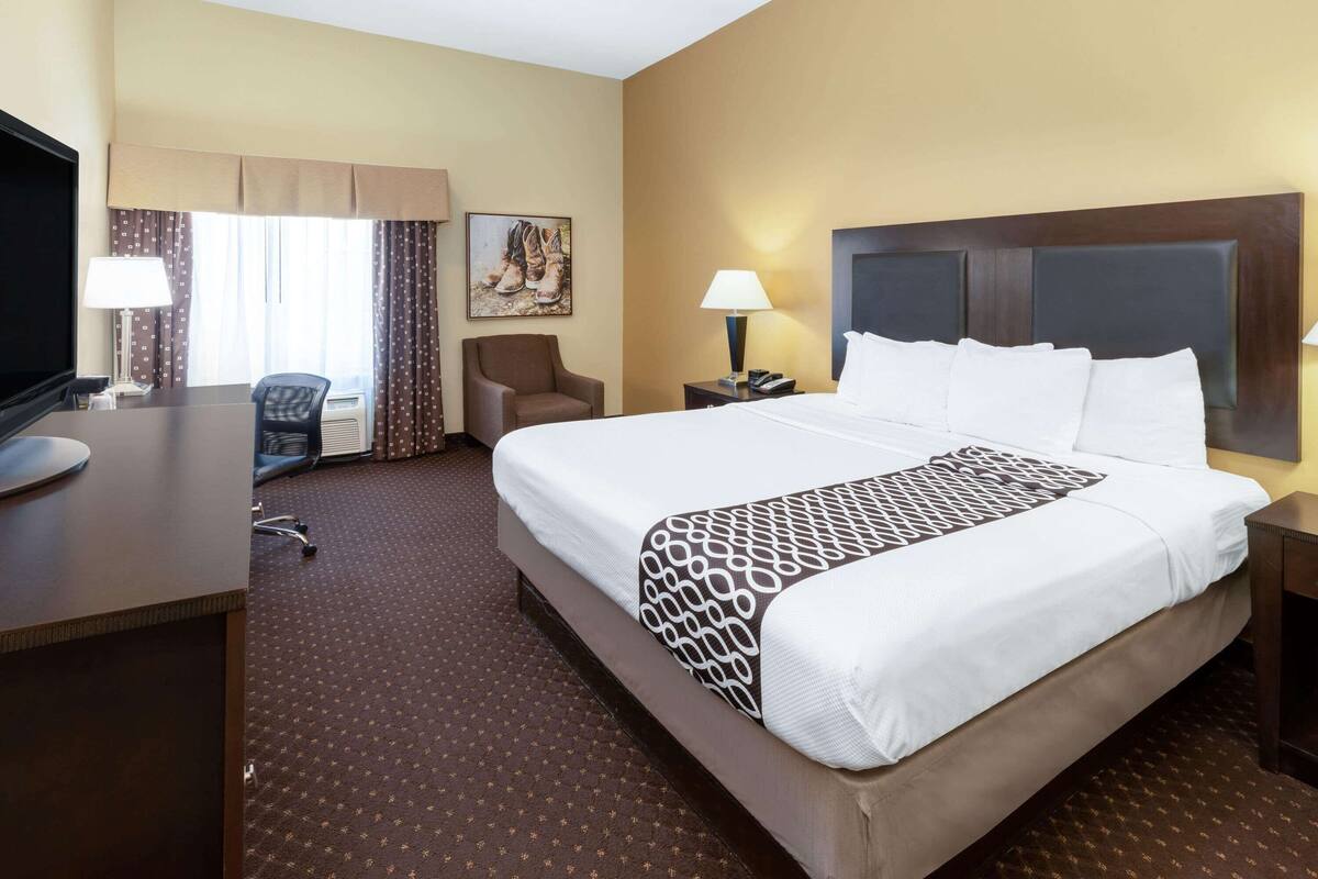 A hotel room with a large bed, a desk, a chair, a TV, and a window with curtains.