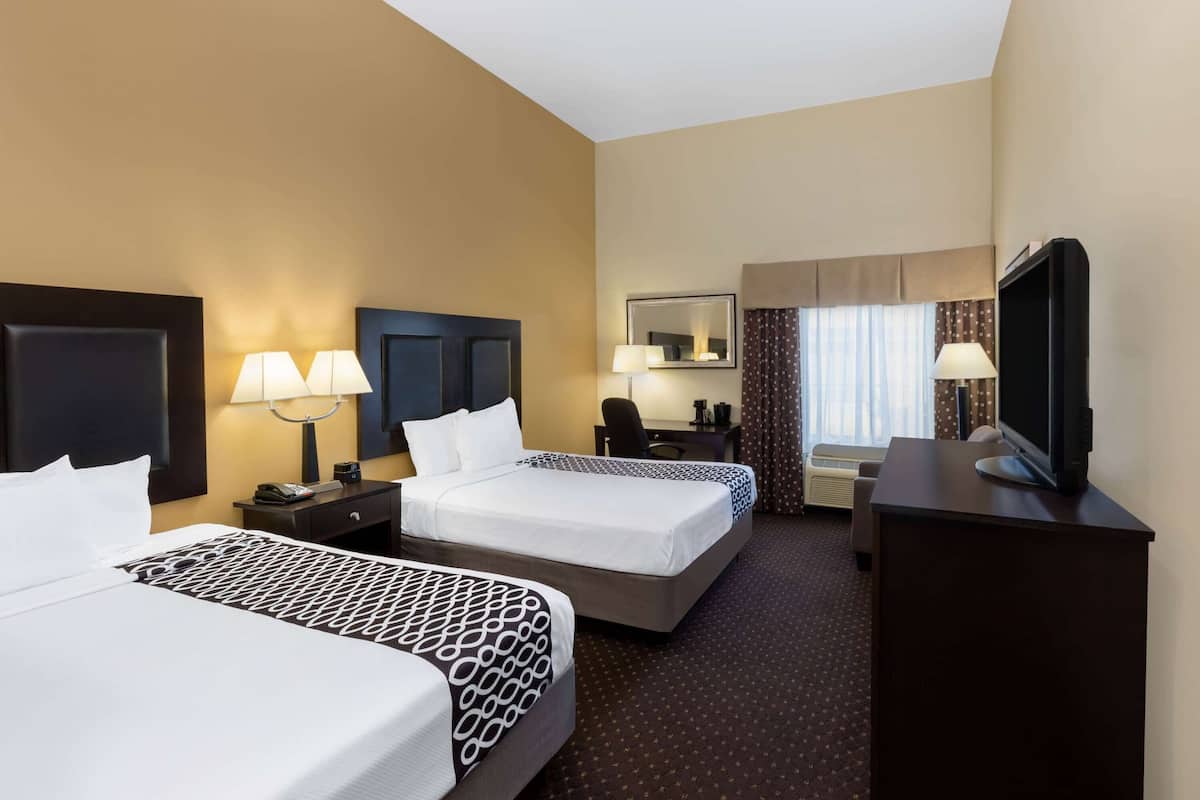 A hotel room with two beds, a desk, a television, and a mirror.