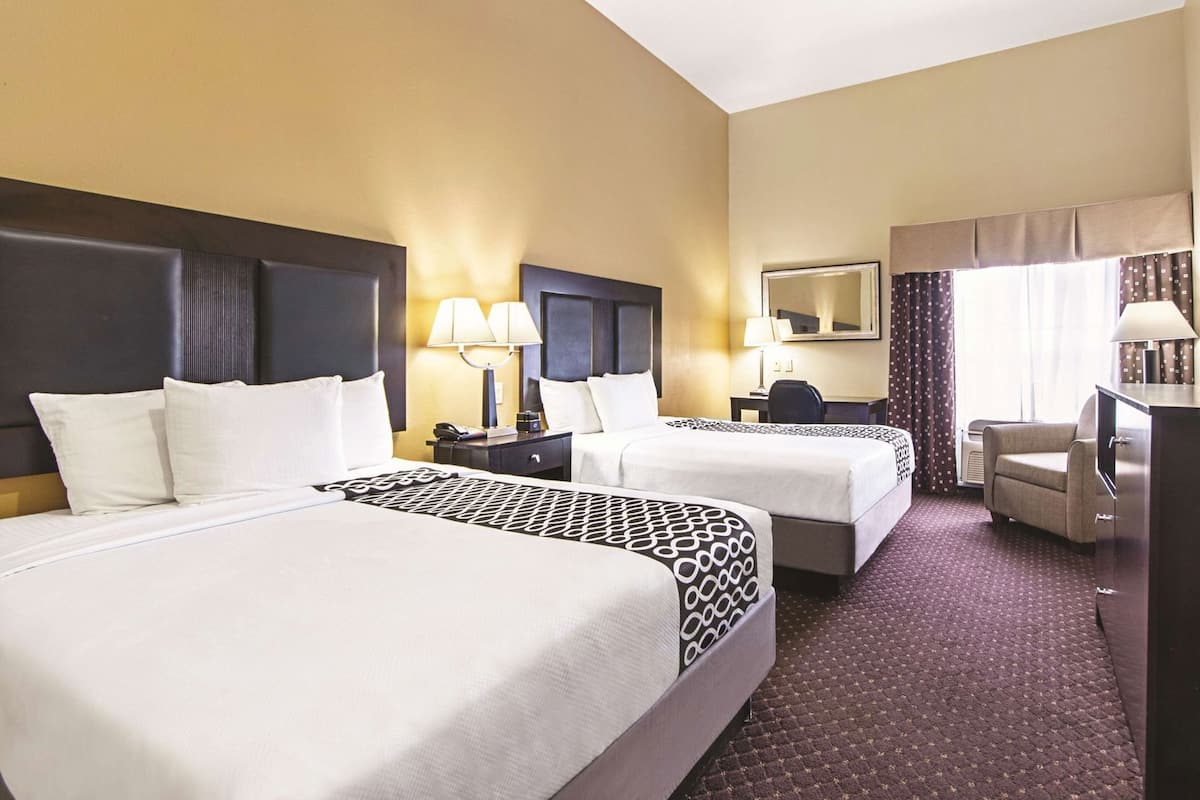 A hotel room with two beds, a desk, a chair, a TV, and a large mirror.