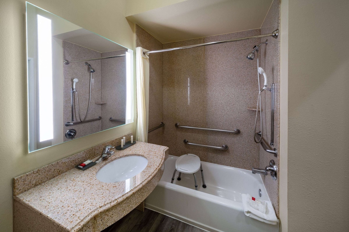 A bathroom with a sink, mirror, shower, and a small stool.