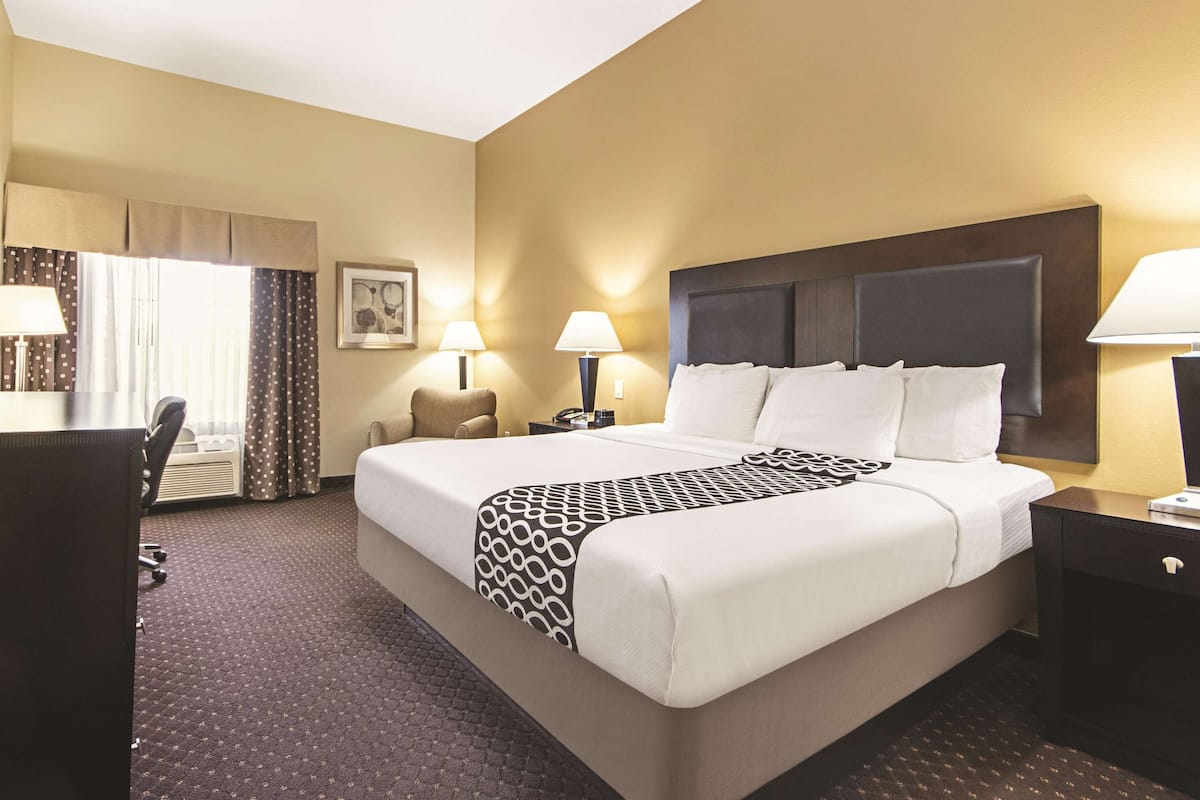 A hotel room with a large bed, two bedside lamps, a desk with a chair, and a window with curtains.