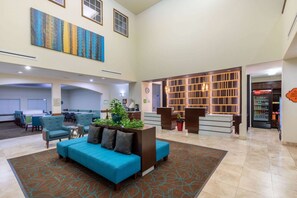 A spacious lobby with a blue sofa, a reception desk, a Coca-Cola refrigerator, and a large abstract painting on the wall. - La Quinta Inn & Suites by Wyndham Houston New Caney (New Caney)