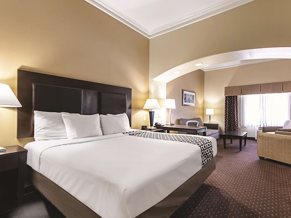 A hotel room with a large bed, a desk, two chairs, a lamp, and a window with curtains. - La Quinta Inn & Suites by Wyndham Houston New Caney (New Caney)