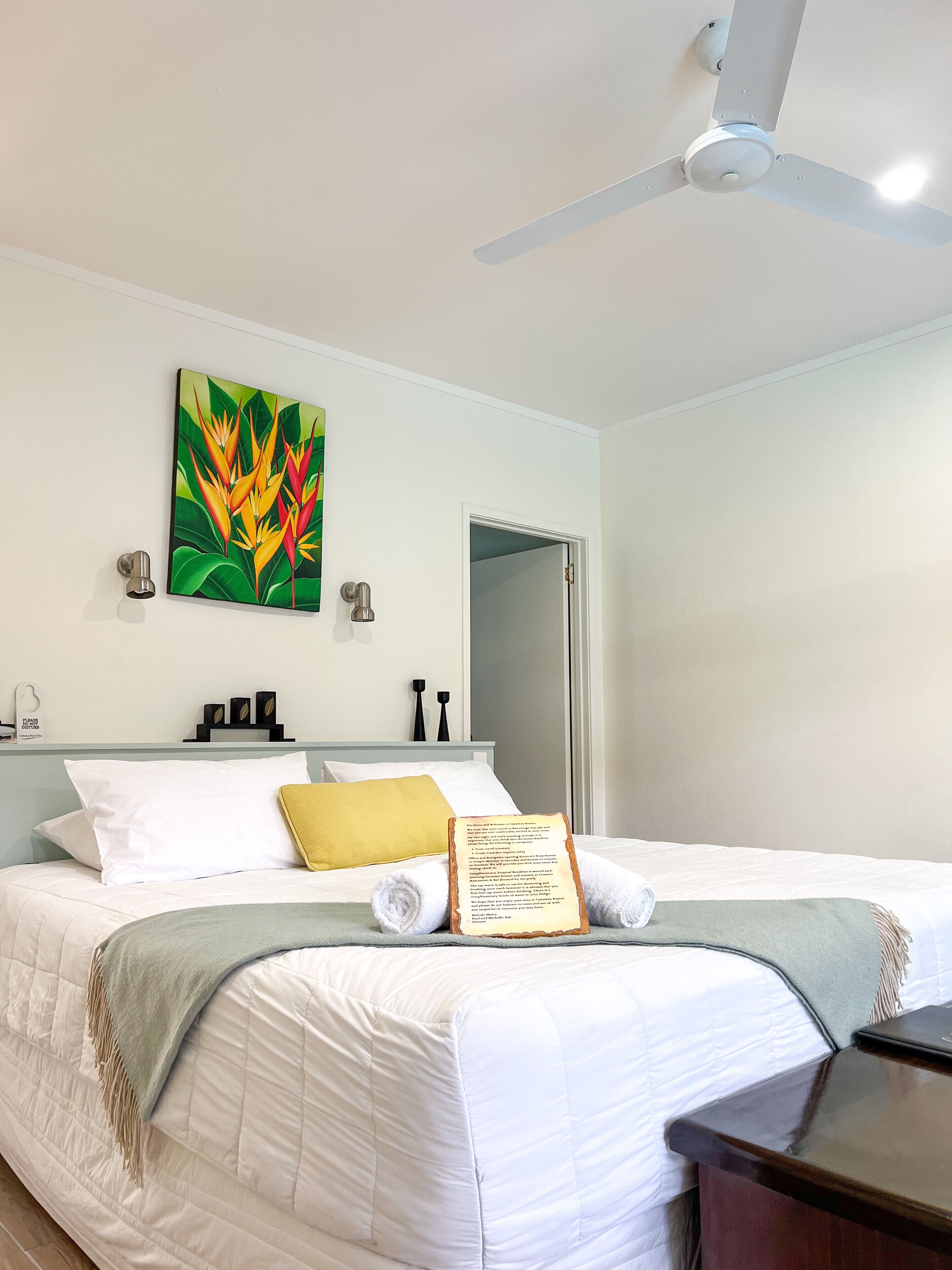 Une chambre d’hôtel avec un lit, un ventilateur de plafond, un tableau et une porte.