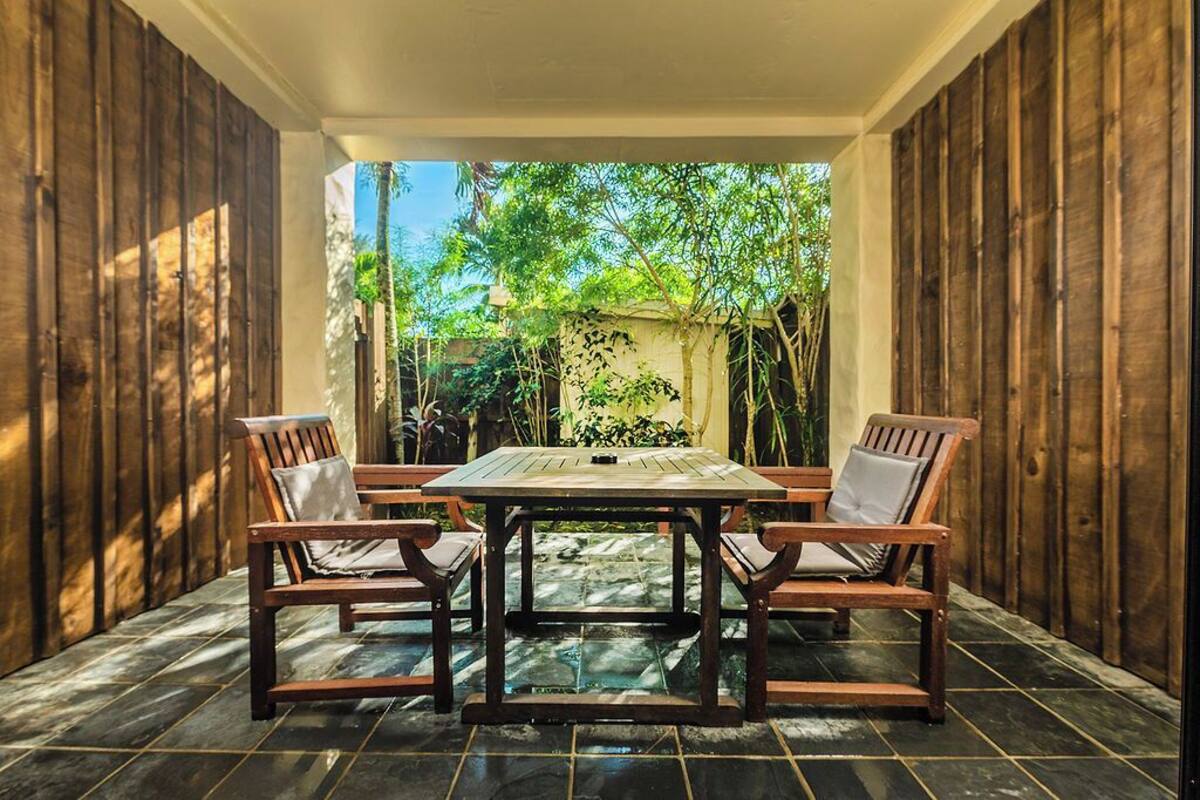 A patio with a wooden table and chairs, surrounded by a wooden fence and greenery.