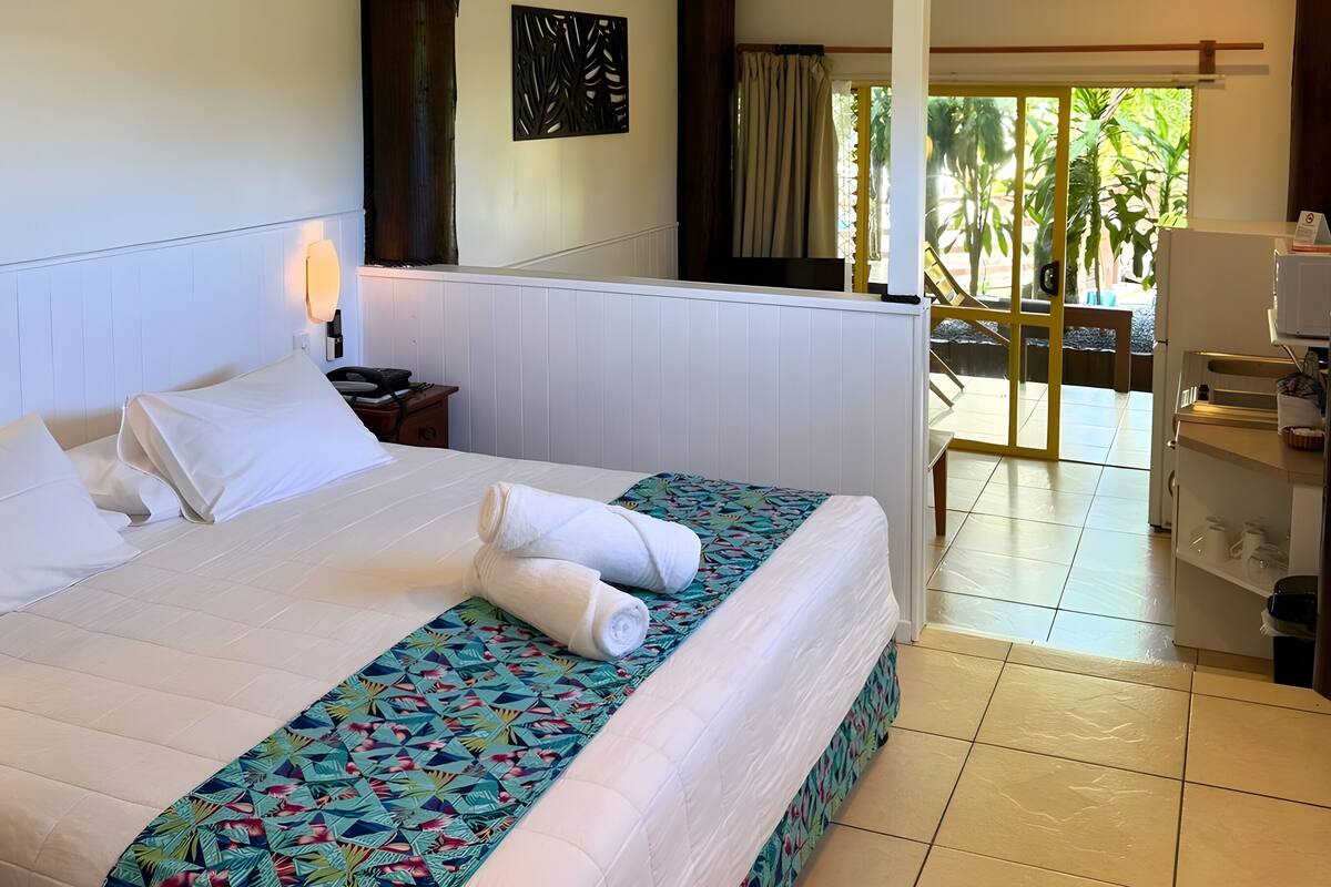 A hotel room with a large bed, a ceiling fan, a nightstand, and a view of the outdoors.