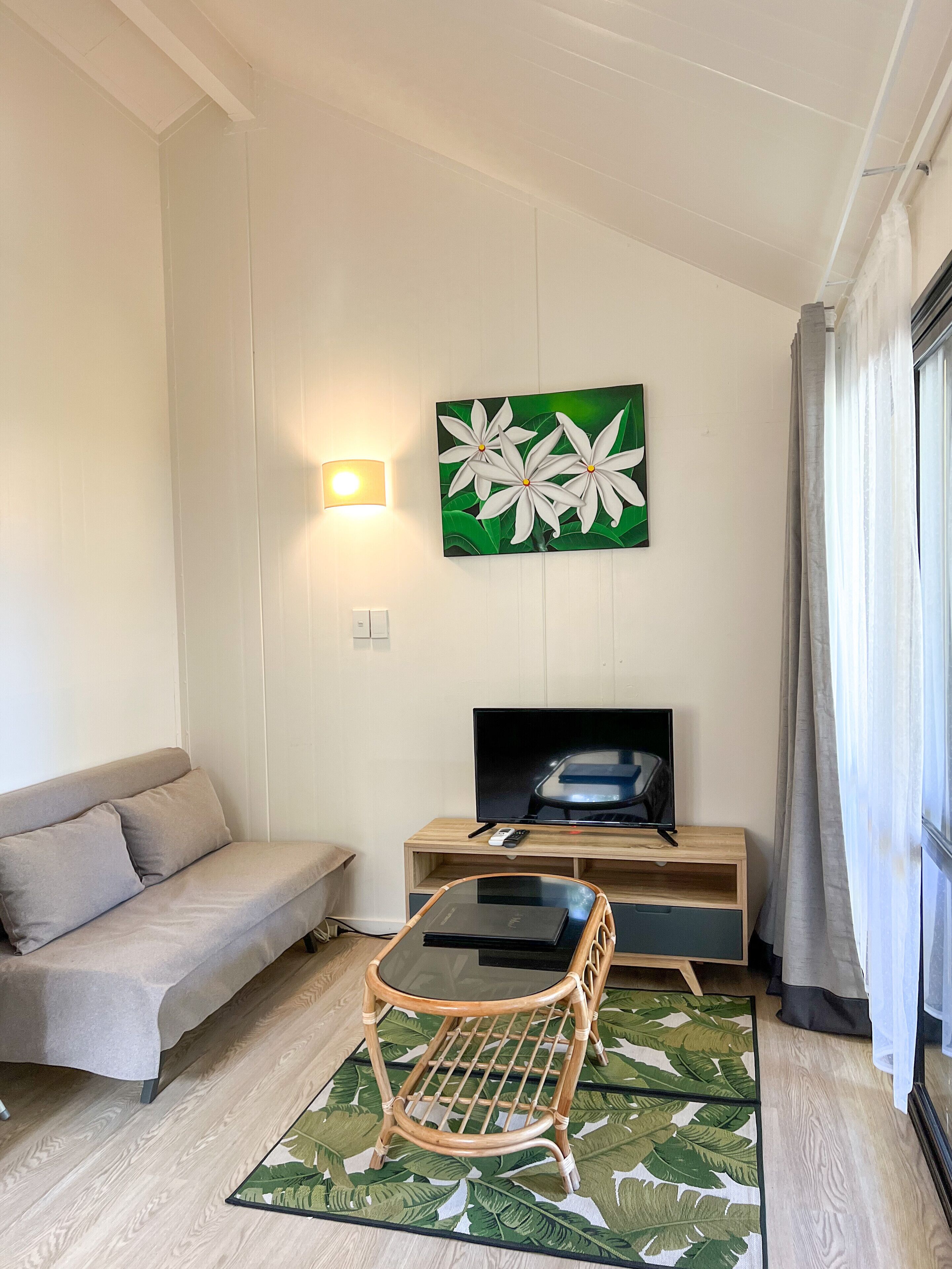 A modern living room with a sofa, a TV, a wicker chair, and a green leaf-patterned rug.
