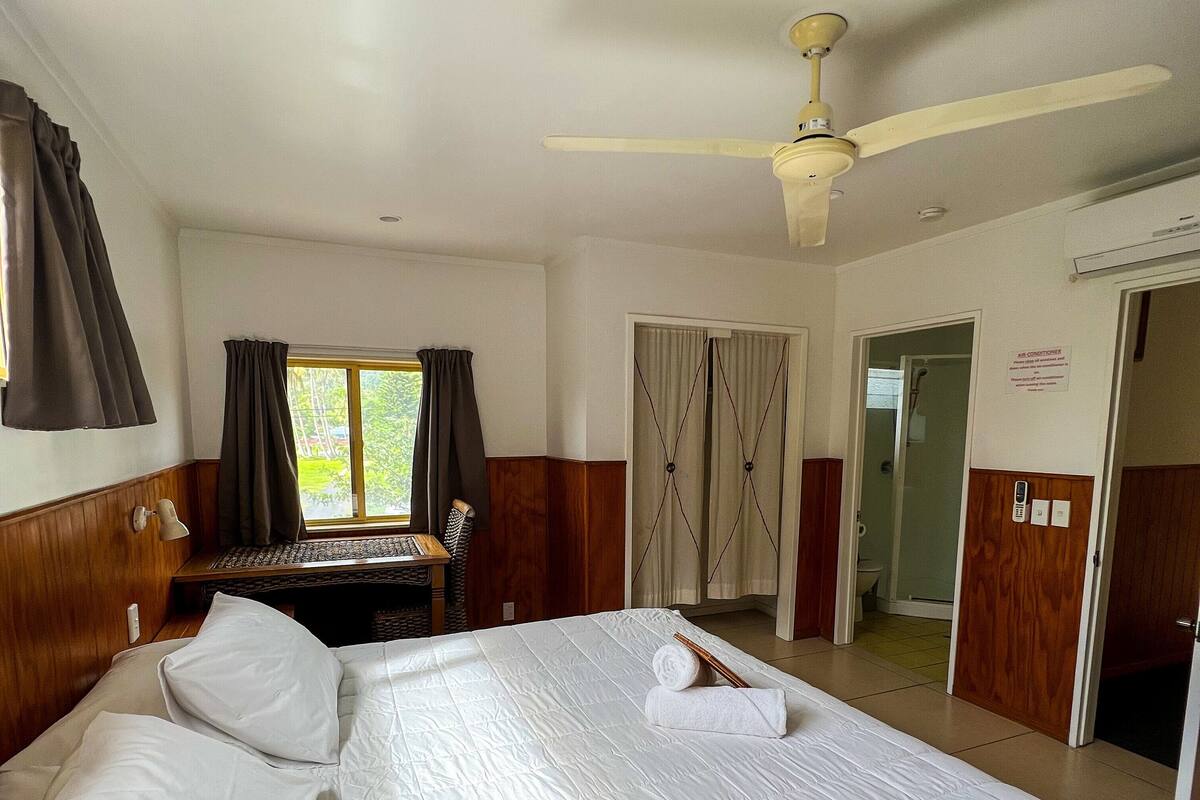 A hotel room with a large bed, a desk, and a ceiling fan.