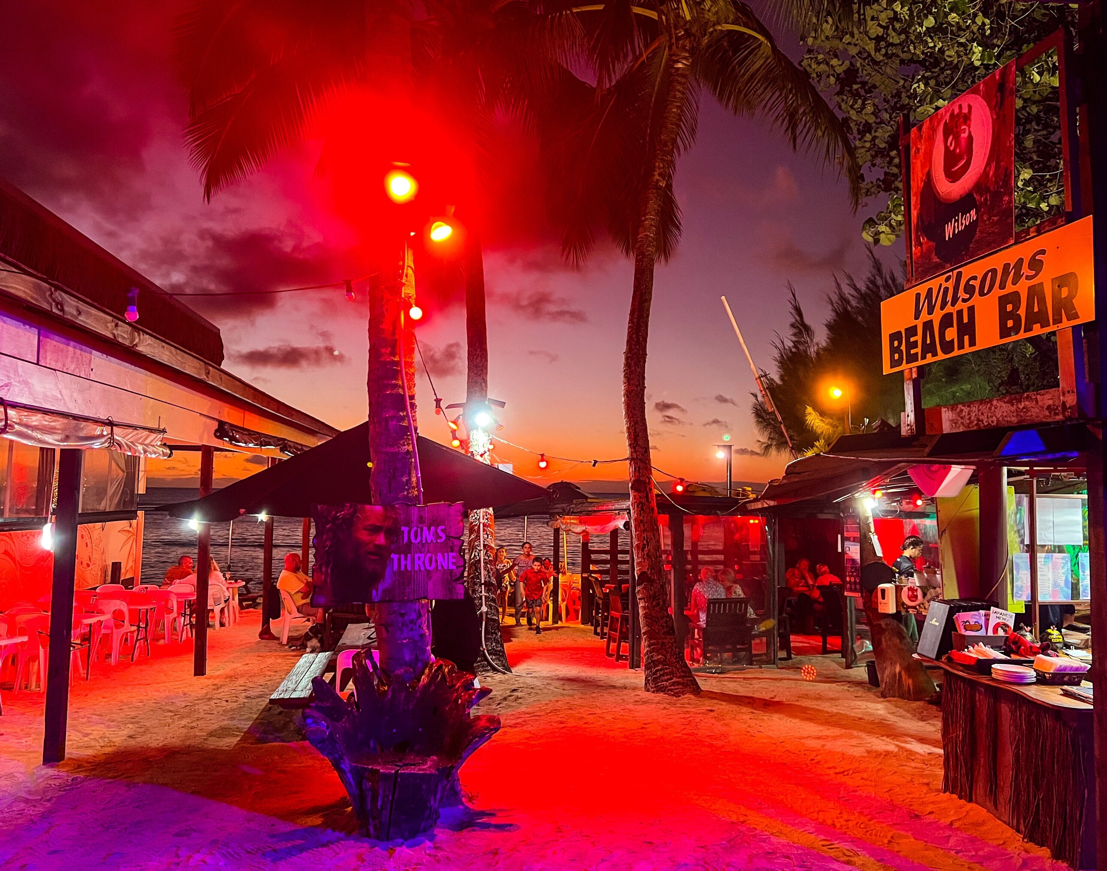 A beach bar with outdoor seating and palm trees.