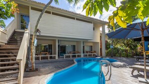 En swimmingpool med en træterrasse, et overdækket siddeområde og en trappe op til en etage over.