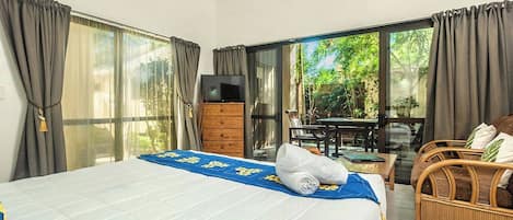 A hotel room with a bed, a TV, a wooden dresser, and a balcony with a table and chairs.
