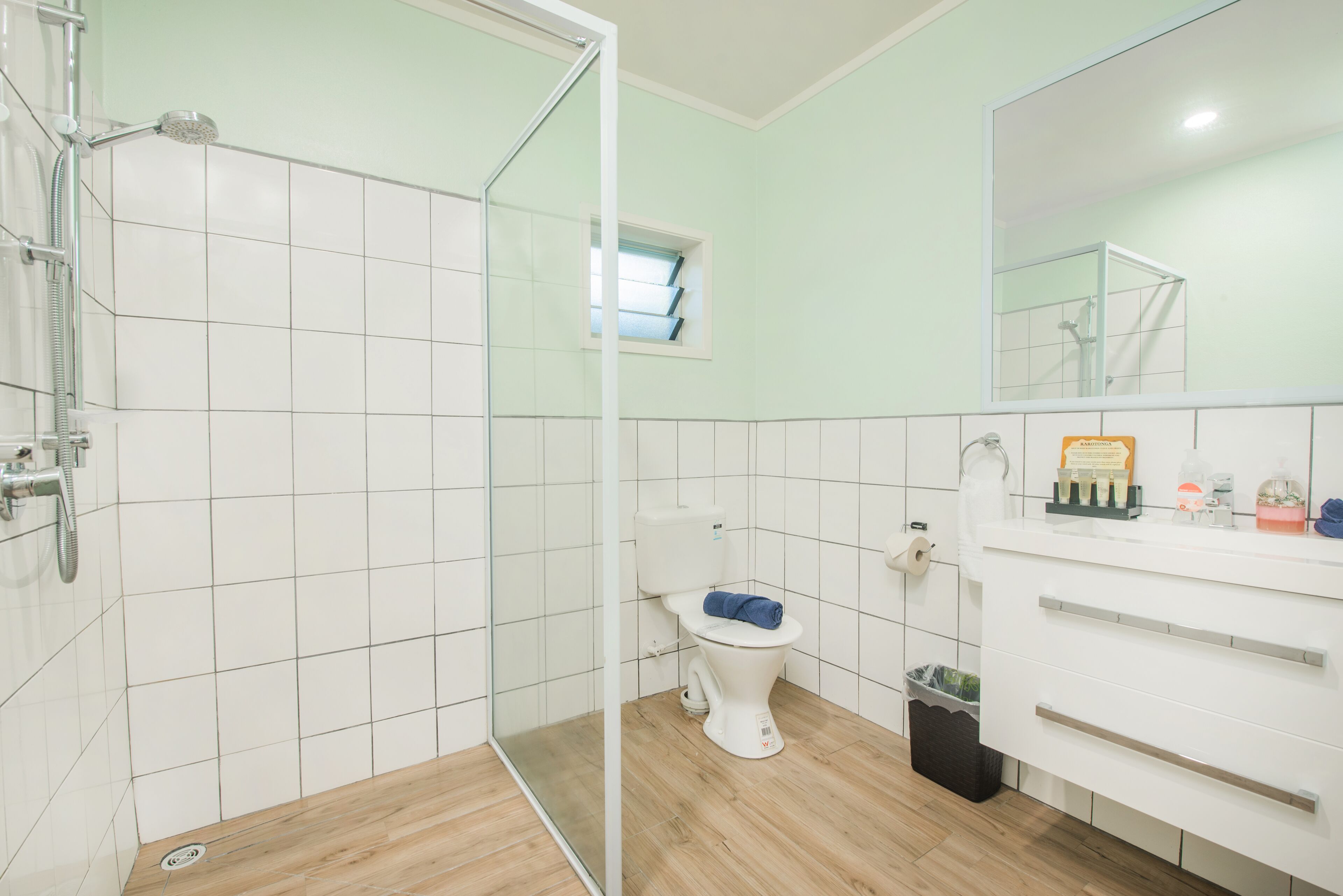 A bathroom with a glass shower enclosure, a toilet with a blue towel, and a sink with toiletries.