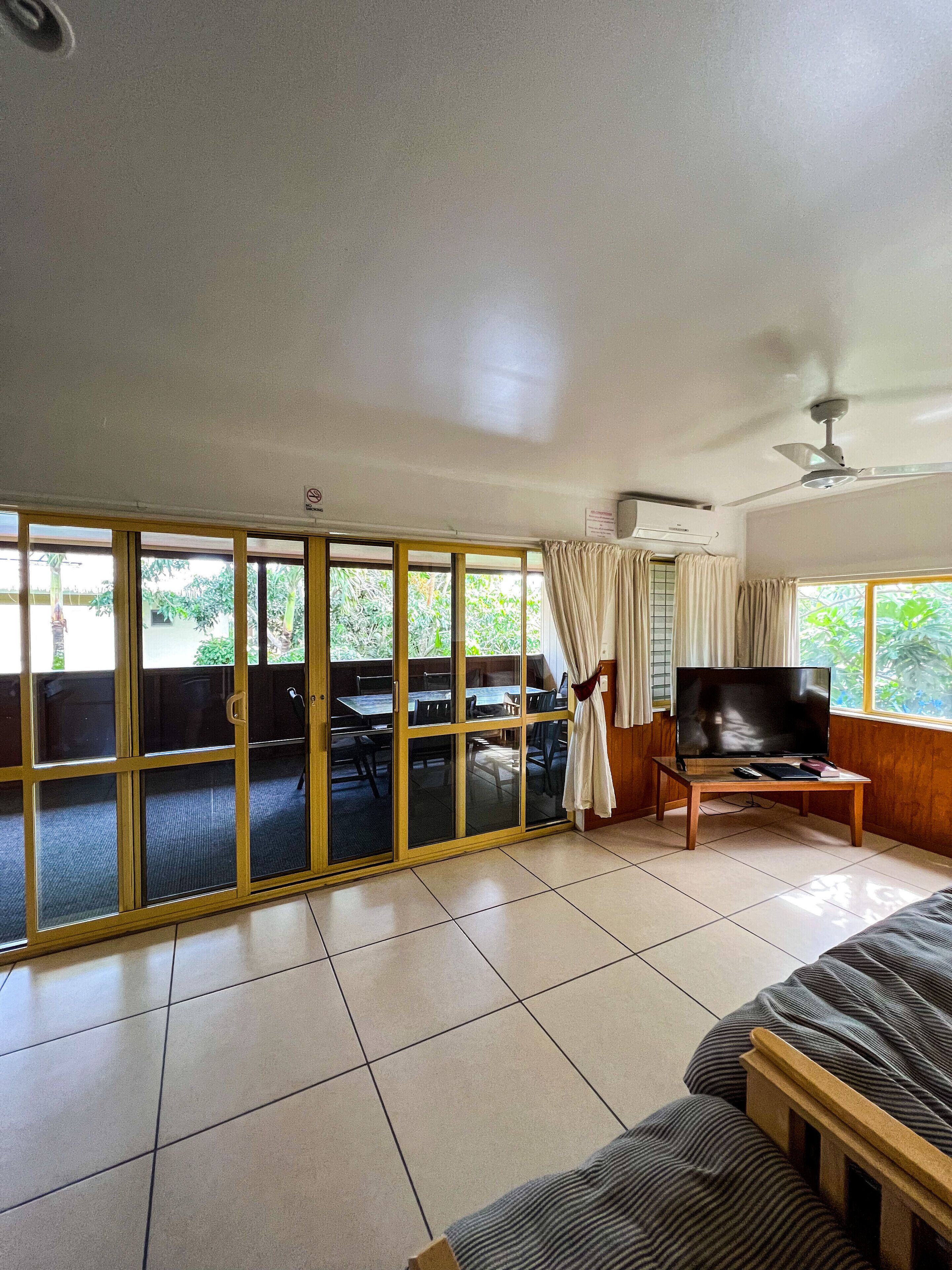 A room with a sliding glass door leading to an outdoor area, a ceiling fan, a flat-screen TV on a wooden stand, and a sofa.
